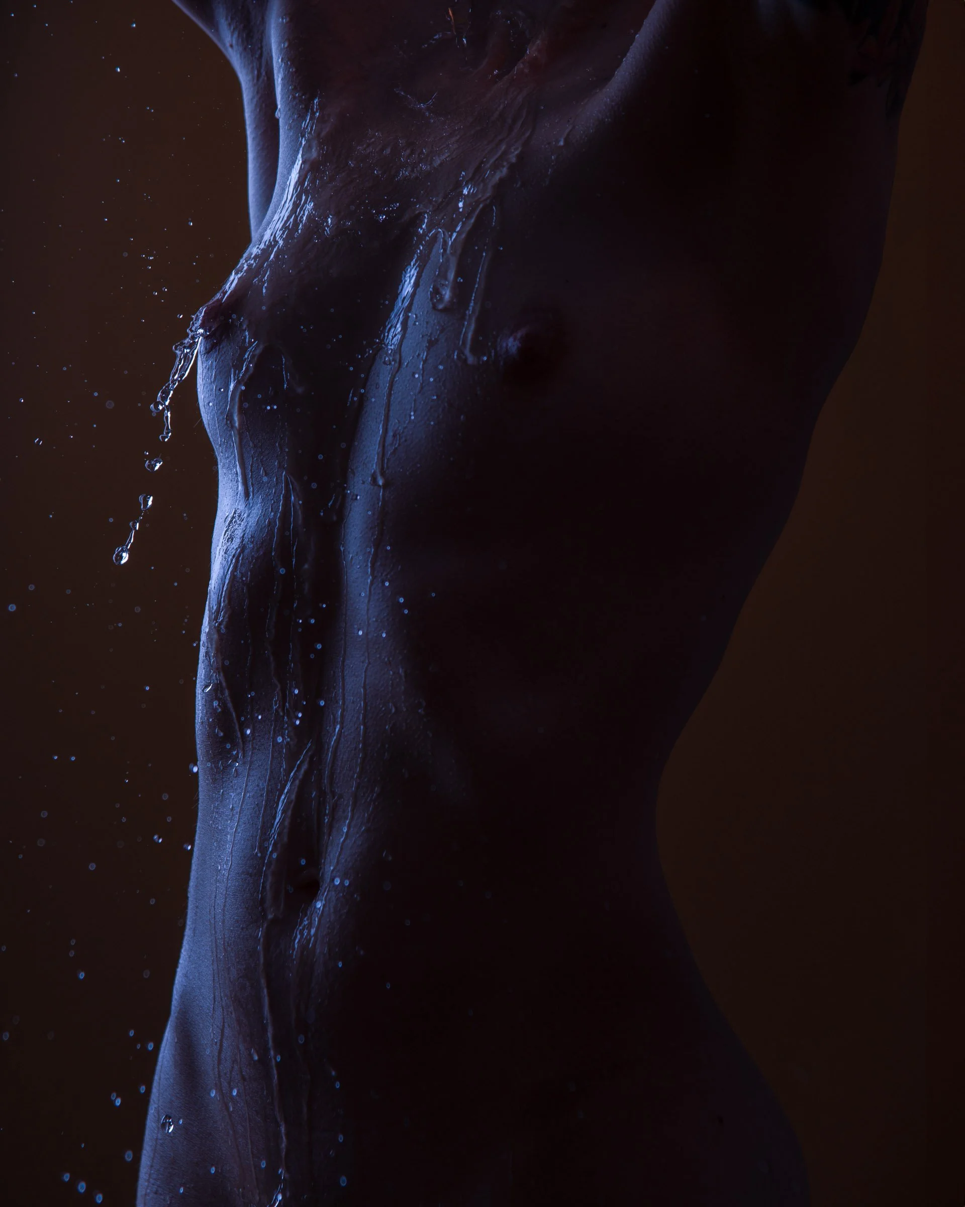 Close-up of a human torso with water droplets on the skin, illuminated with blue lighting, and a dark background.