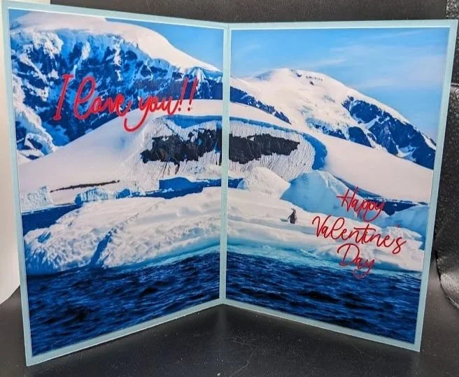A folded Valentine’s Day card featuring a snowy mountain landscape with an iceberg, snow, and water, with red handwritten-style text saying "I love you!!" on the left side and "Happy Valentines Day" on the right side.