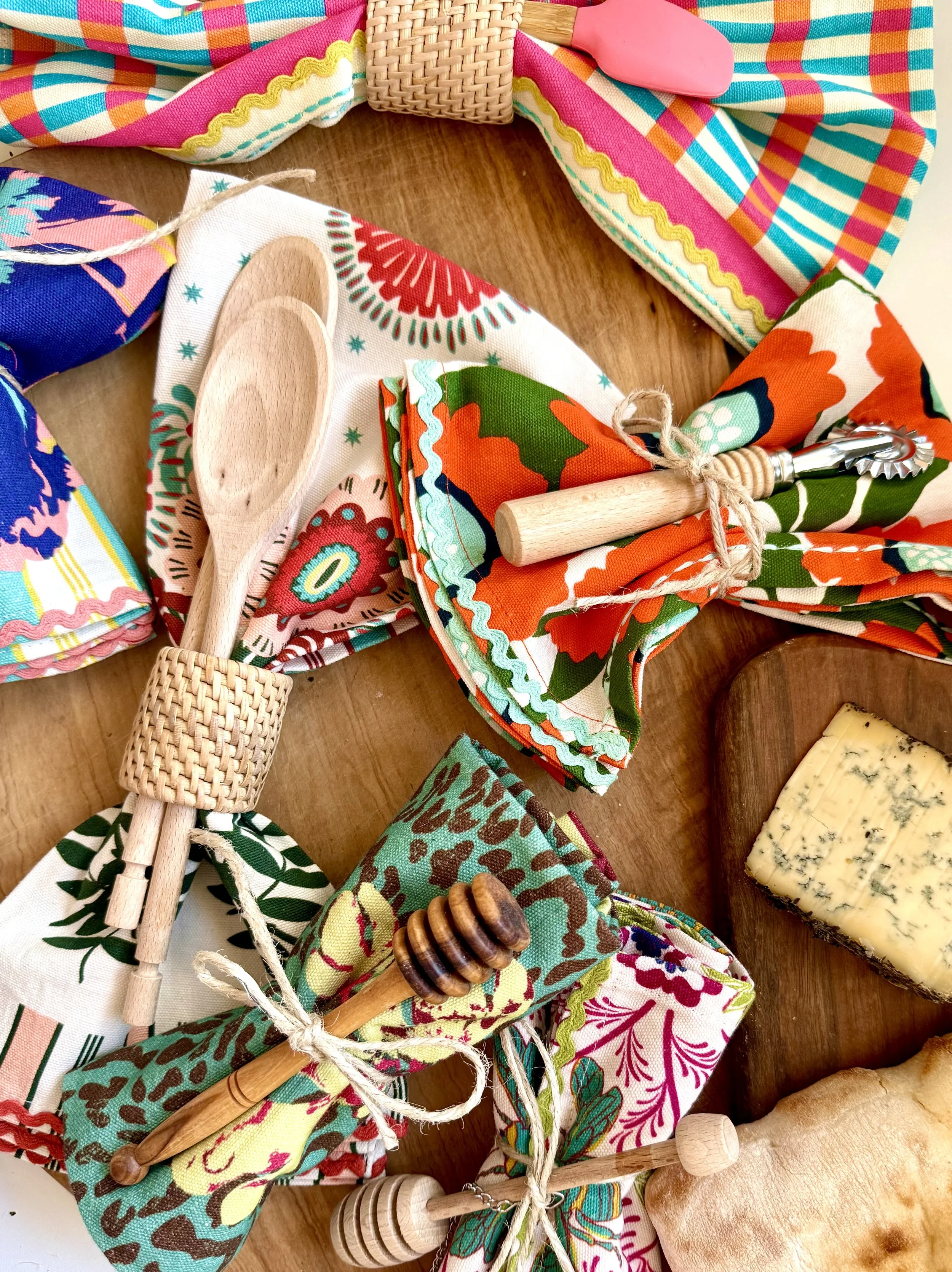 Colorful maximalist cotton dish towels rolled with wooden spoons and rattan rings on a wooden board, kitchen home decor by artist Lynette Reed