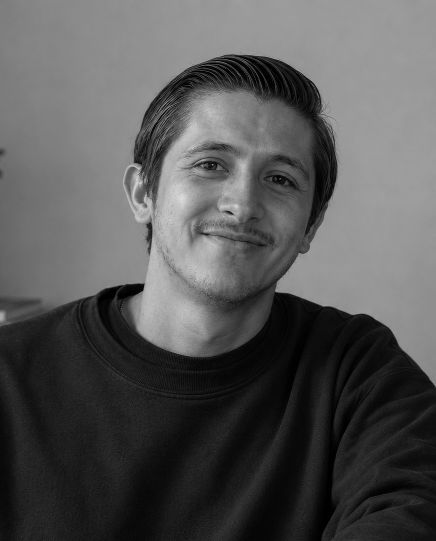 Black and white portrait of a young man with a slight smile, wearing a dark sweatshirt, with a plain background.