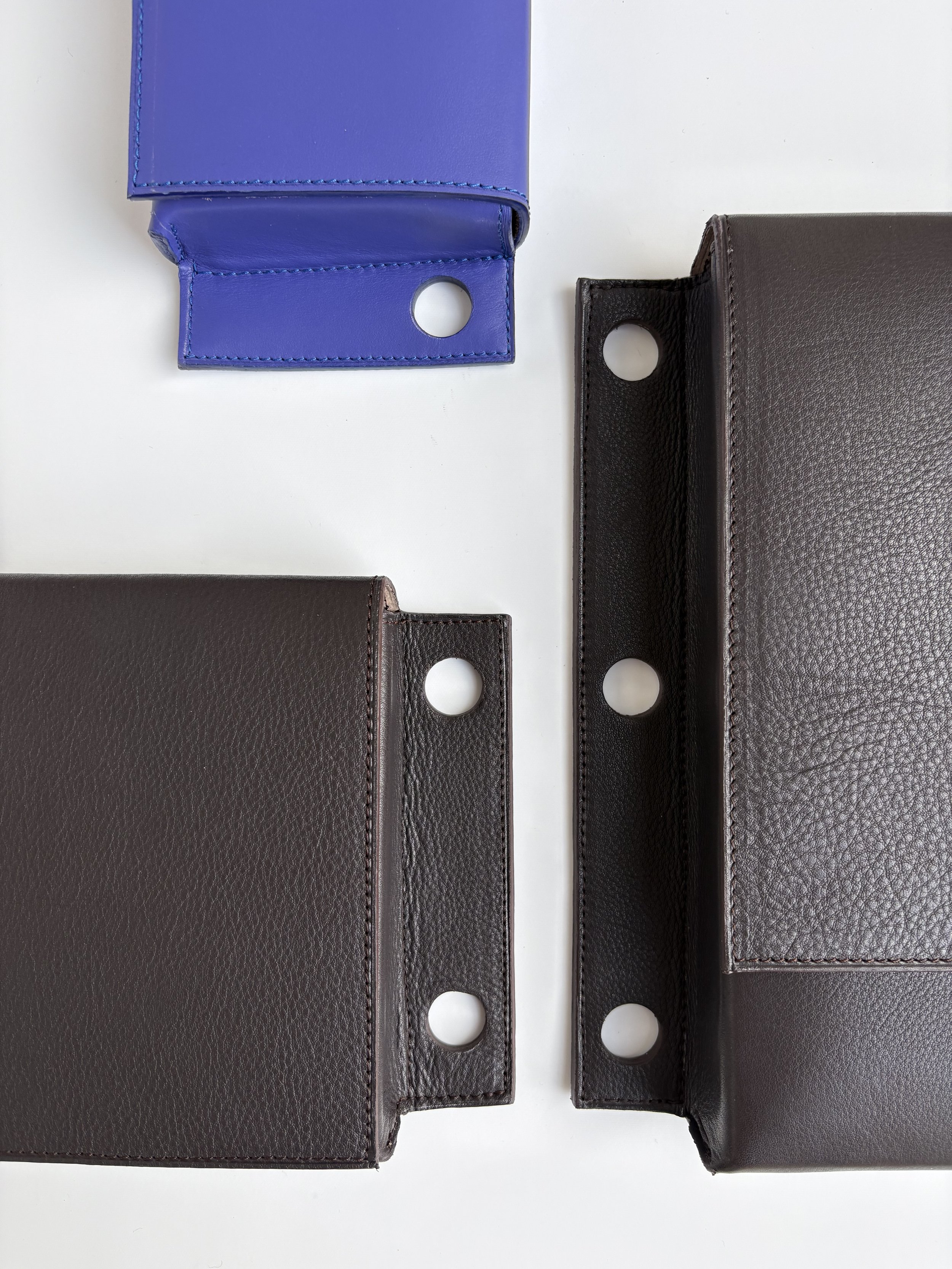 Foto van drie leren tassen in verschillende kleuren: bruin, donkerbruin en blauw, met ronde gaten om draagriem door te steken
