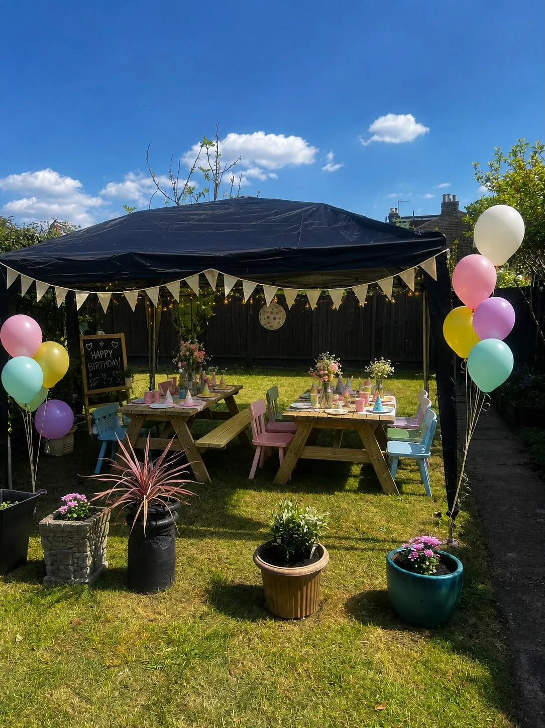 Beautifully styled outdoor children's birthday party in a London garden with pastel balloons, bunting, picnic tables and a Happy Birthday chalkboard.