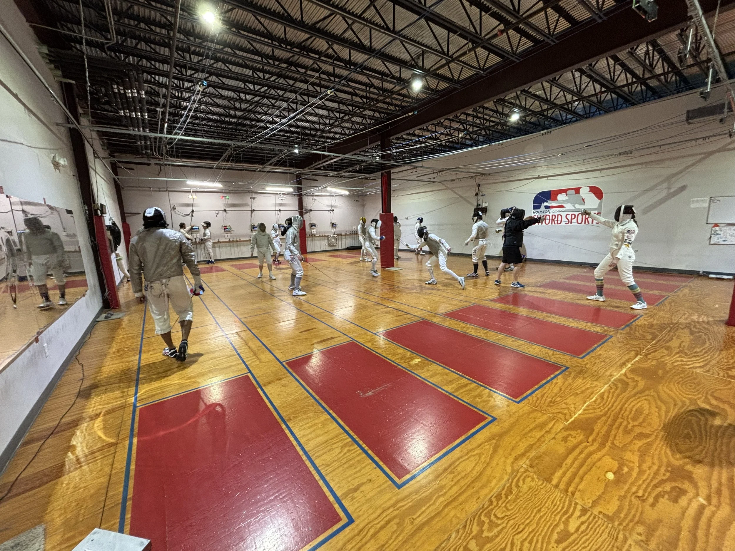 A fencing club full of adult fencers, who are practicing in all three weapons