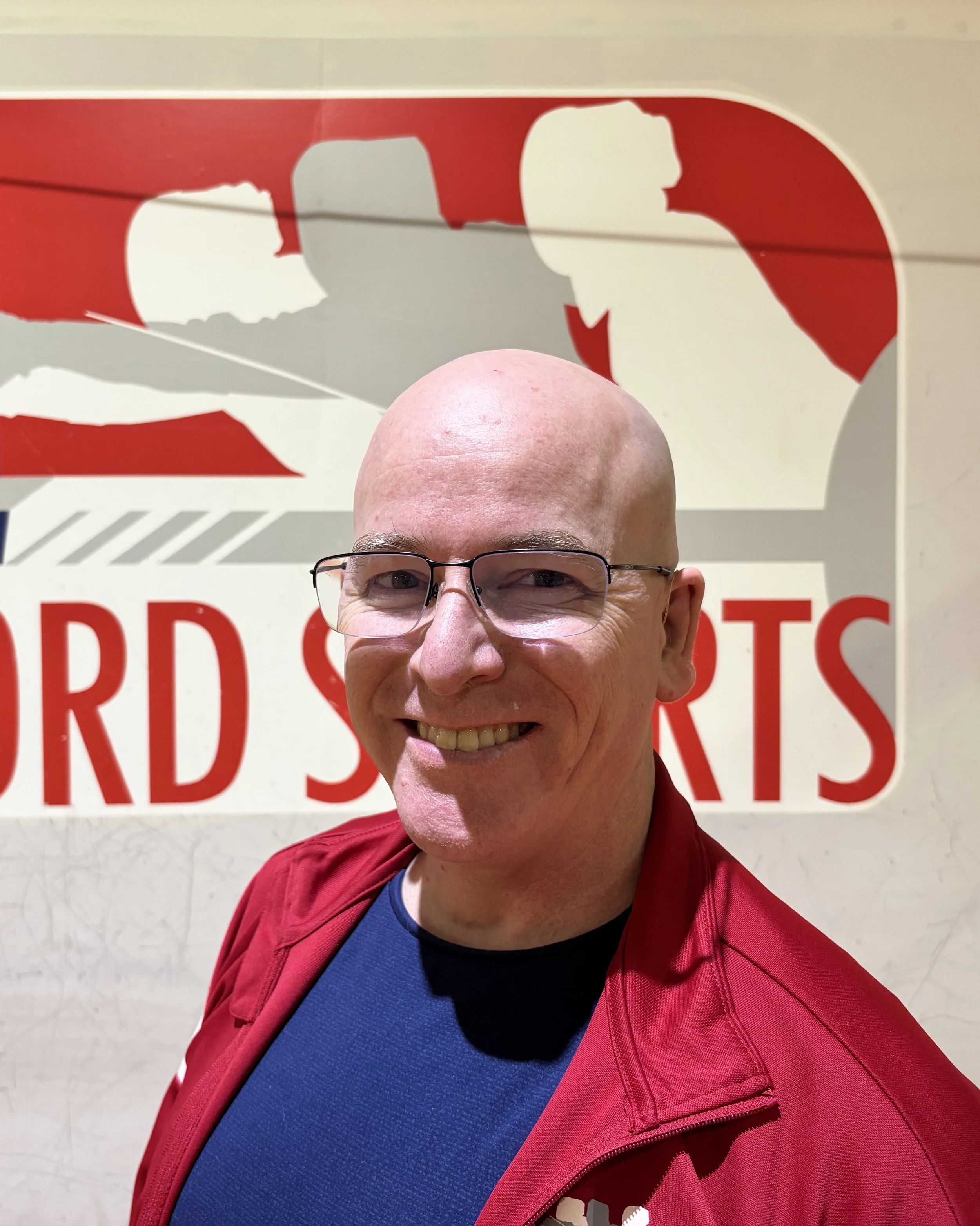 Coach Dan smiling in front of the HSS logo
