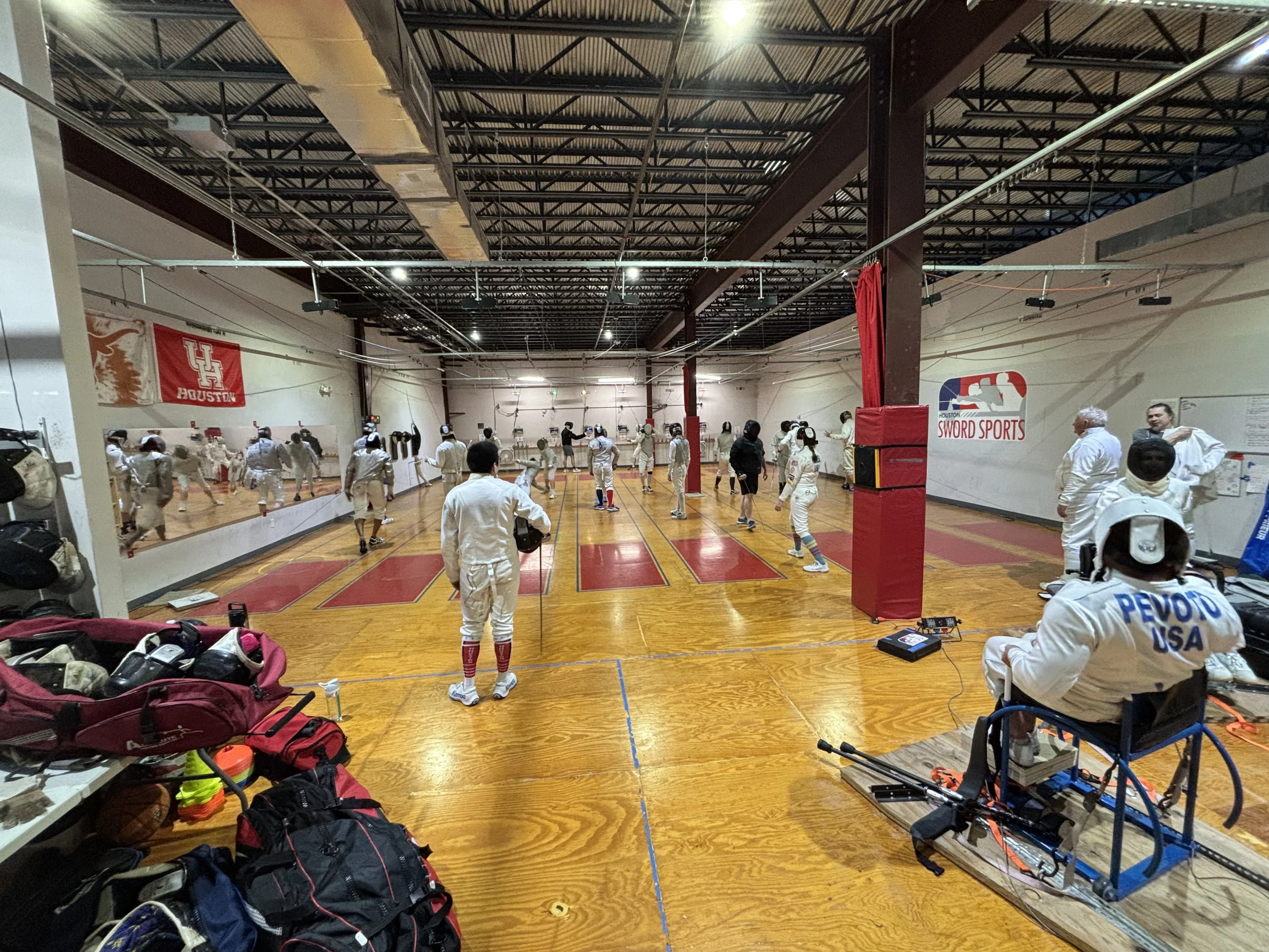 Houston Sword Sports is a fencing club with 8 strips and a wheelchair fencing rig. This photo shows the strips full of fencers in epee, foil and saber.