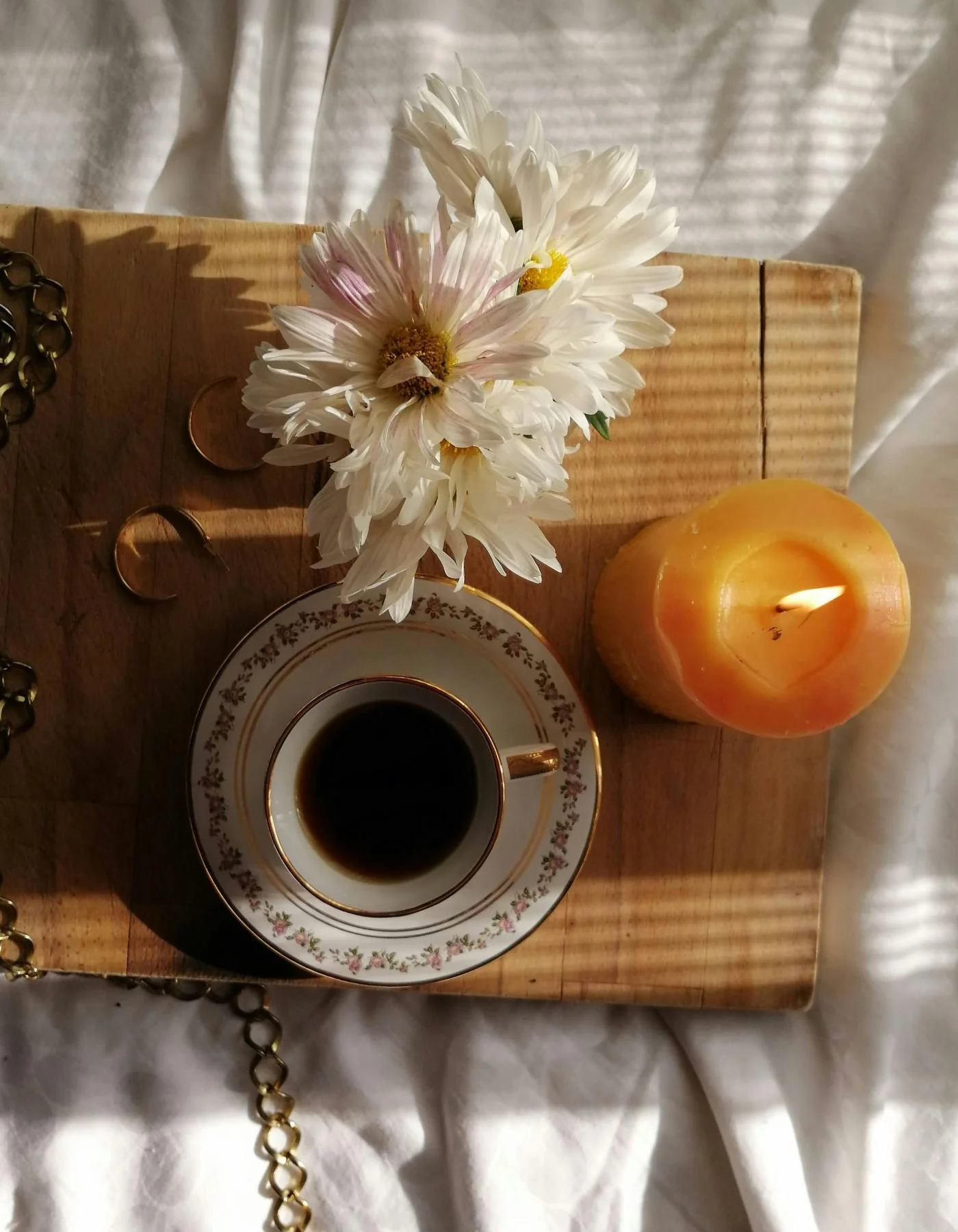 White flowers in a vase, a cup of coffee on a saucer, a lit yellow candle, and jewelry on a wooden tray. Online anxiety therapy across CA & FL serving West Los Angeles.