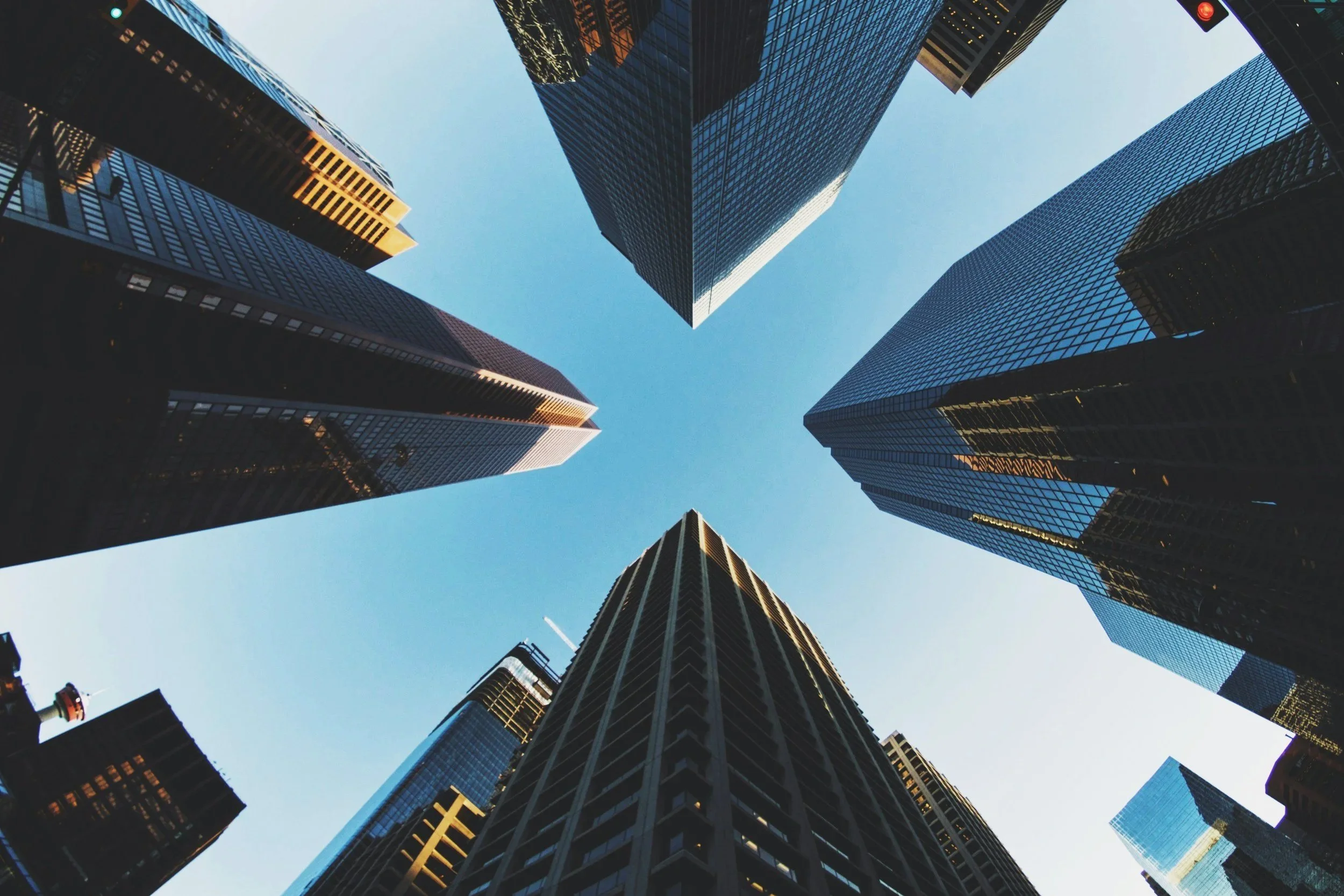 Looking up at tall modern glass skyscrapers in a city, with a clear blue sky in the background.
