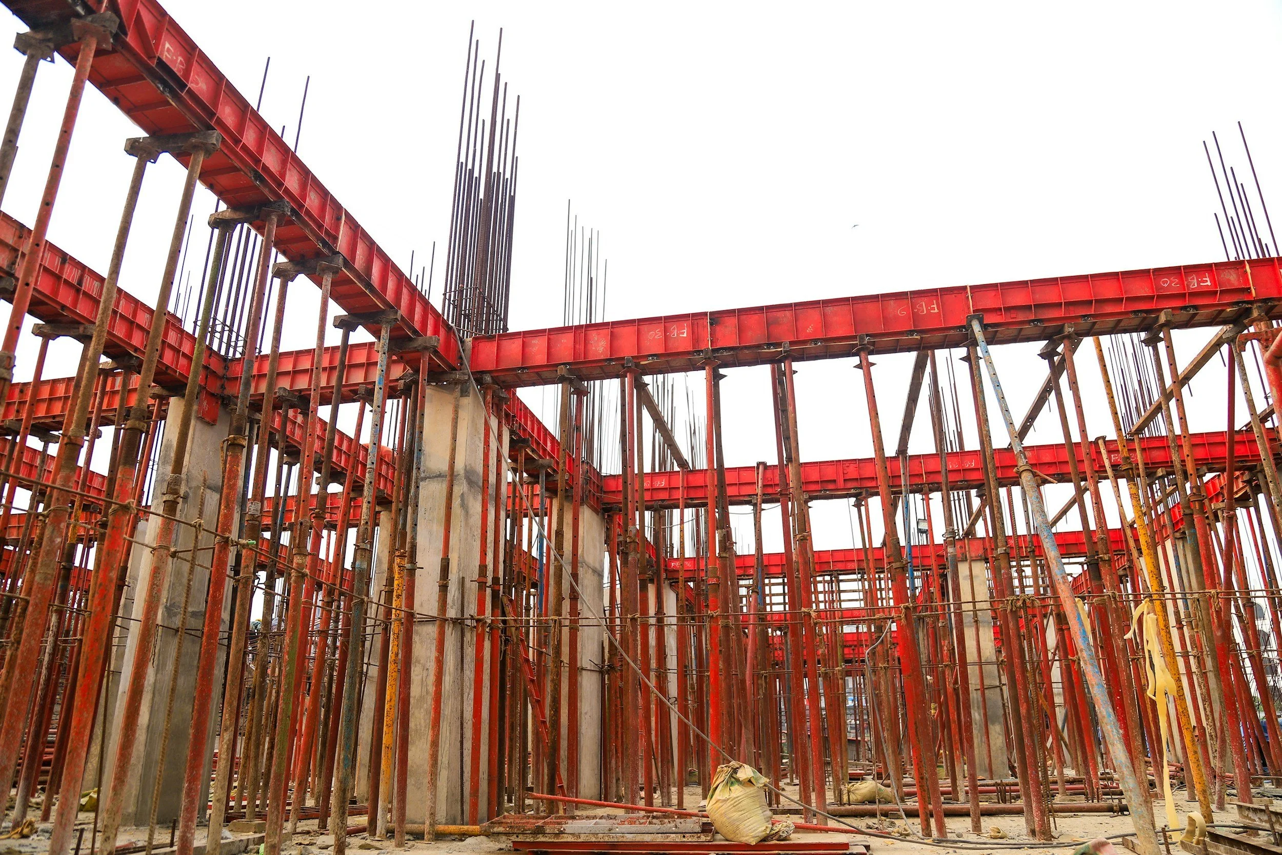 Construction site with red scaffolding and concrete columns under a cloudy sky.