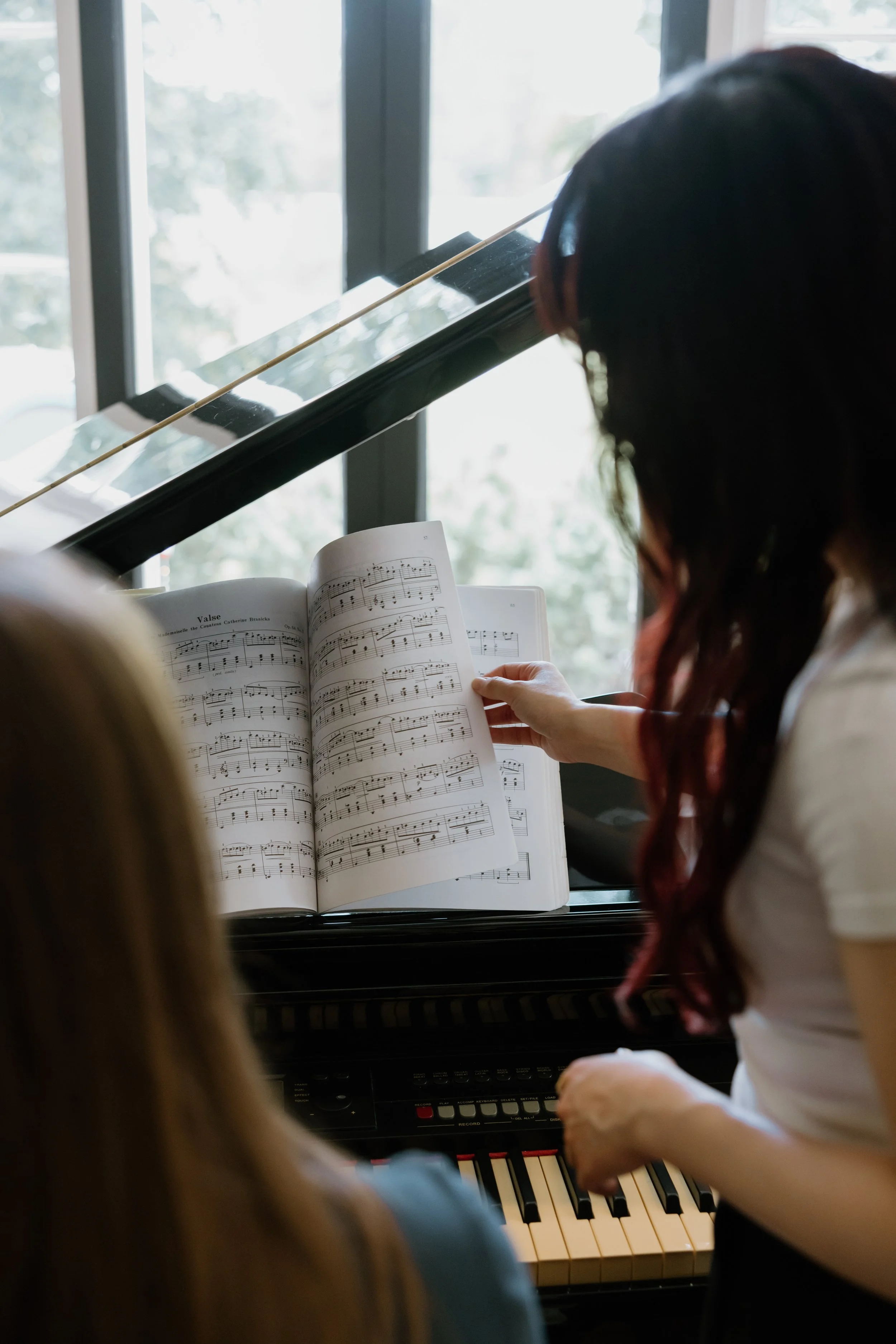 A student playing the piano with sheet music, with help from a teacher under the Royal Conservatory of Music Canada (RCM)