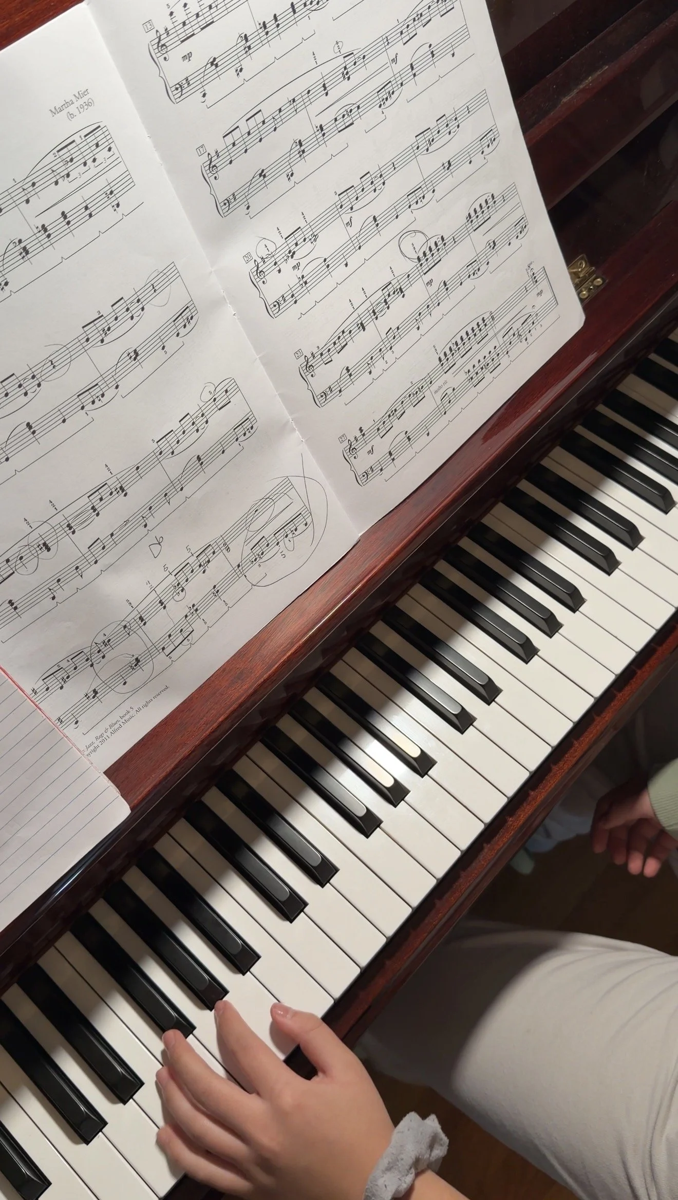 Close-up view of an open sheet music book on a piano, showing musical notes and notation, with a child's hand on the keyboard.