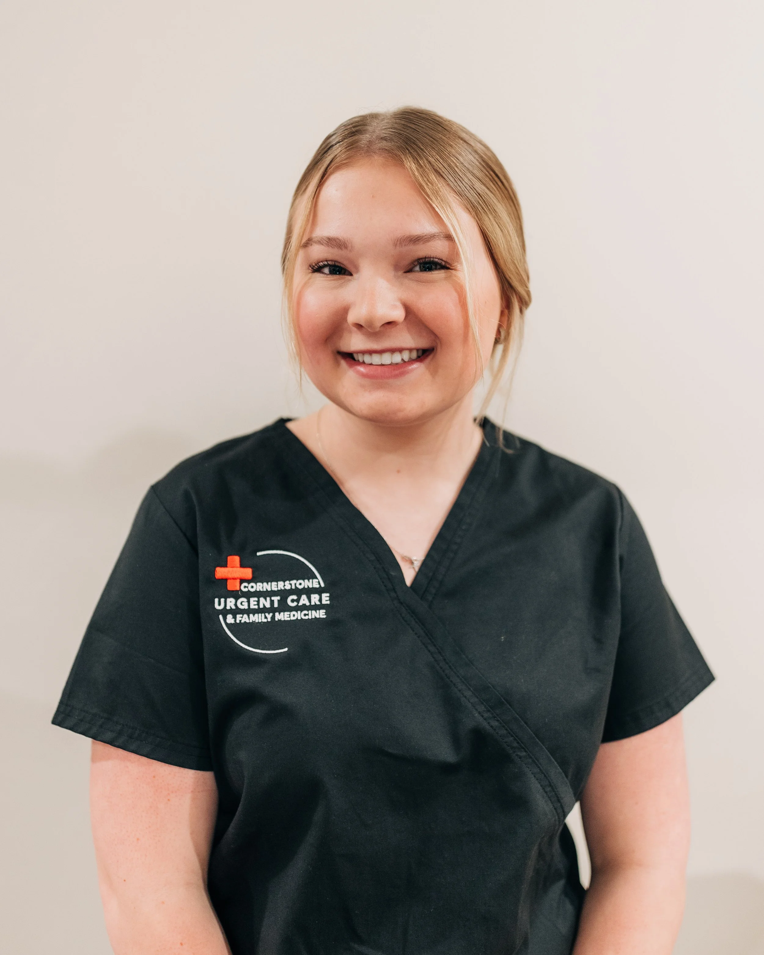 Close-up of a smiling woman wearing a black medical uniform with a logo for Cornerstone Urgent Care & Family Medicine.