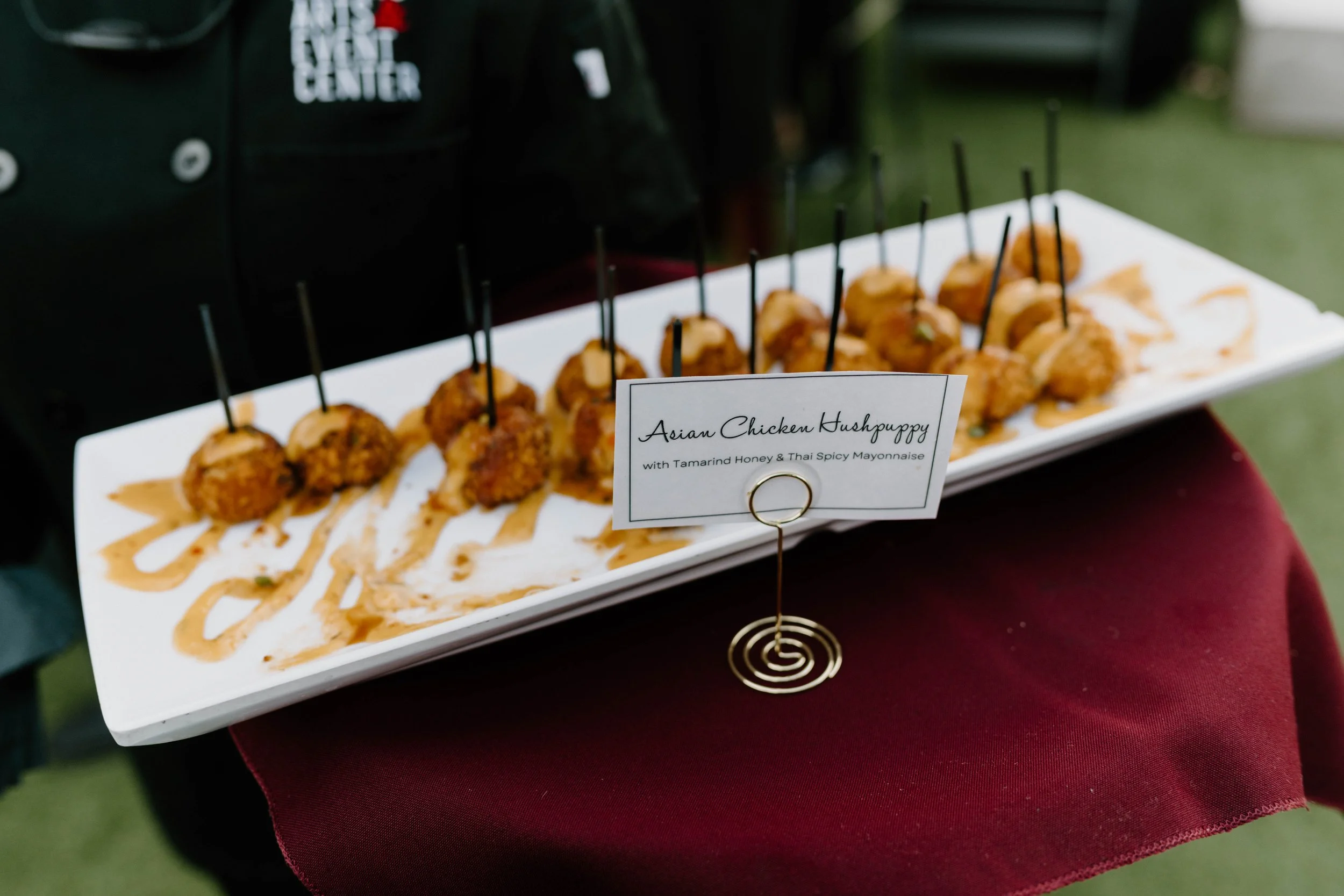 Plate of Asian chicken hushpuppies with tamarind honey and Thai spicy mayonnaise, garnished with sauce and herbs, on a white rectangular plate.