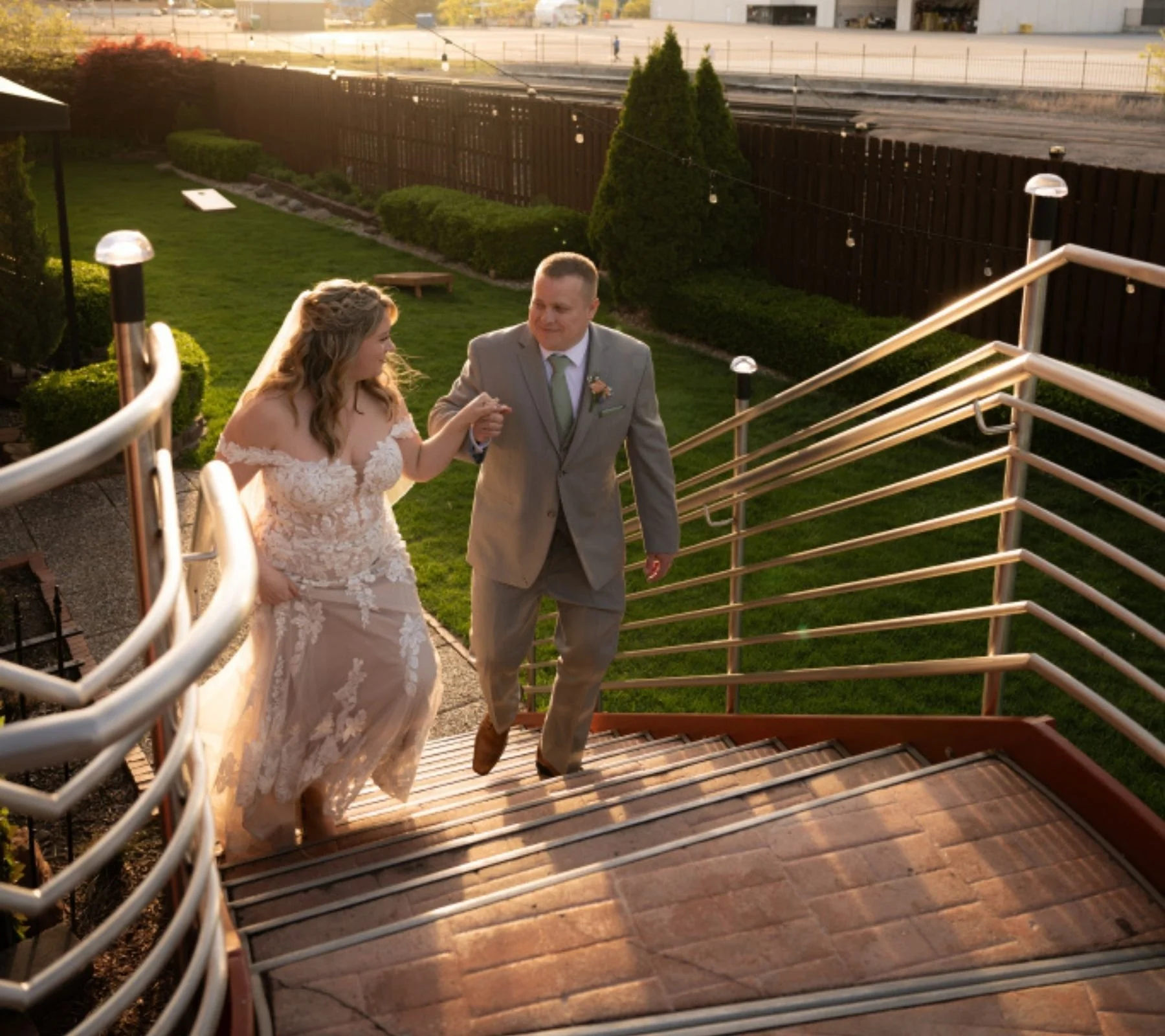 Bride and groom walking up outdoor stairs during sunset, holding hands and smiling.