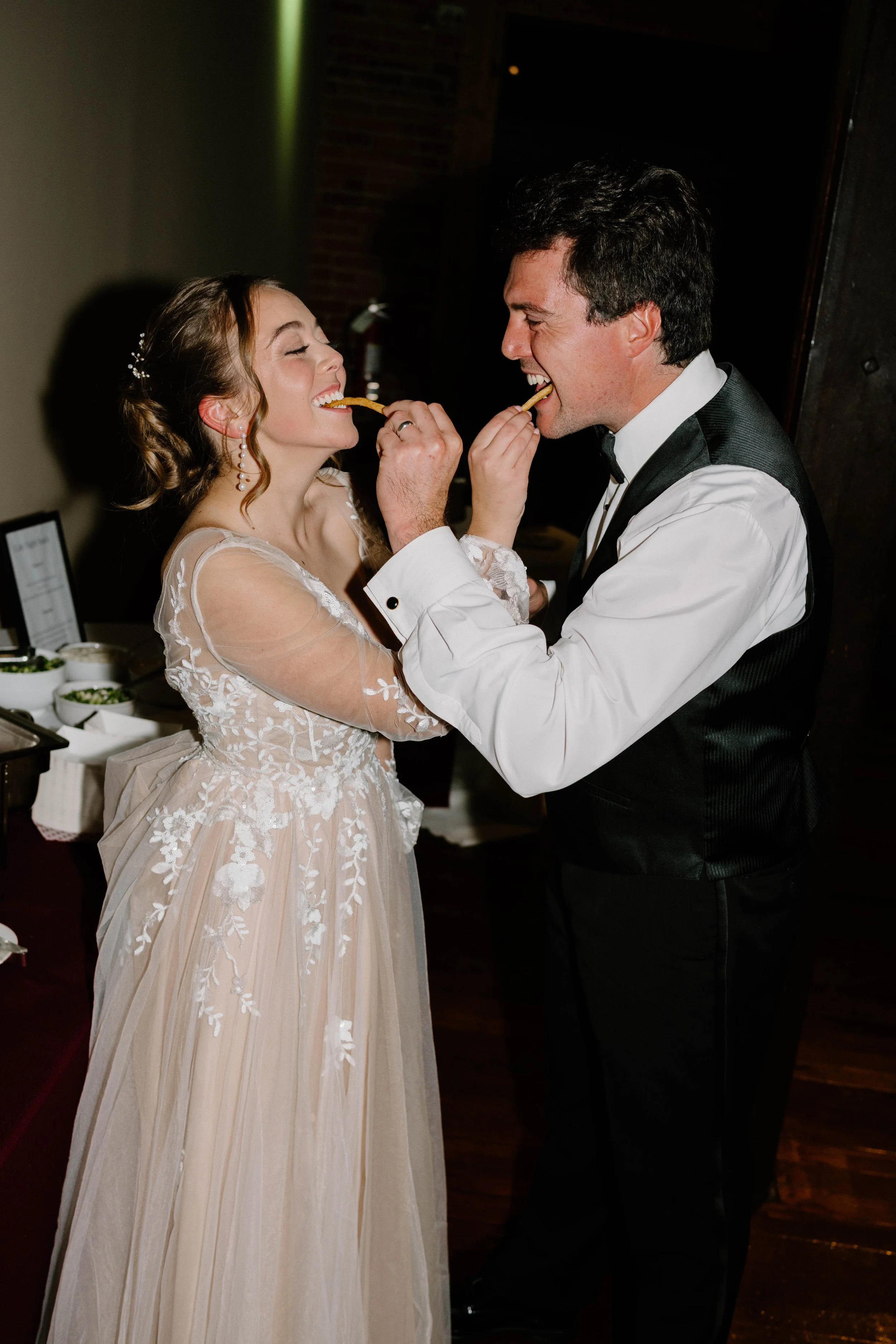 A bride and groom sharing a piece of French fry during their wedding reception.