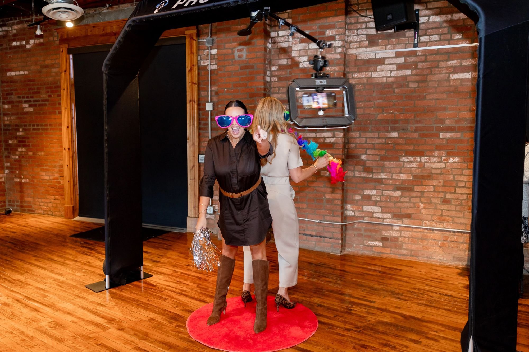 Women at a photo booth with props, one woman pointing at the camera, similar to a party or celebration.