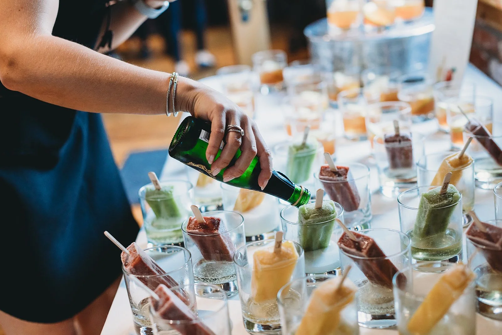 Person pouring soda into colorful popsicles at a party or event.