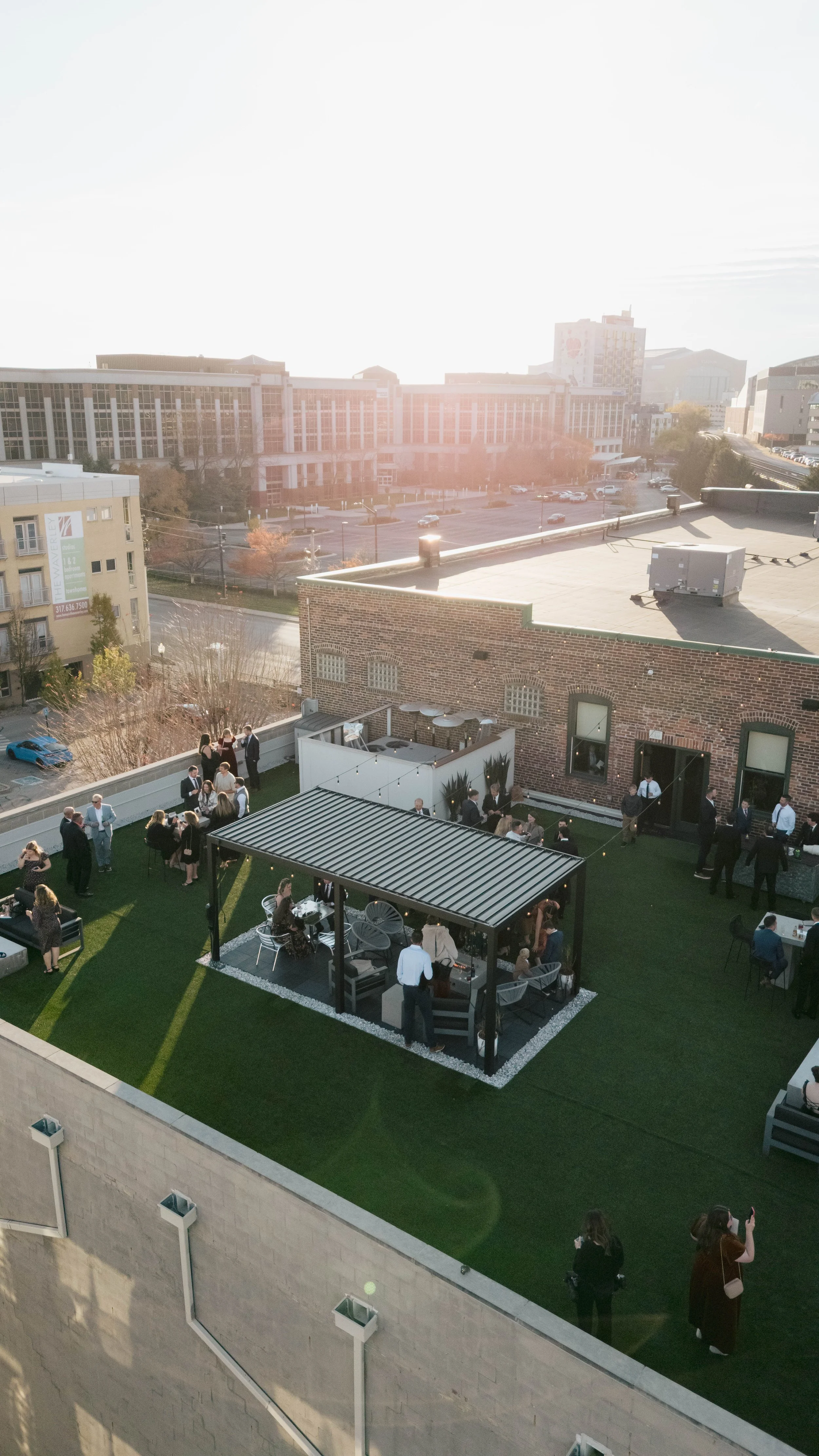 People gathered on a rooftop terrace during a social event in the late afternoon, with a cityscape in the background.