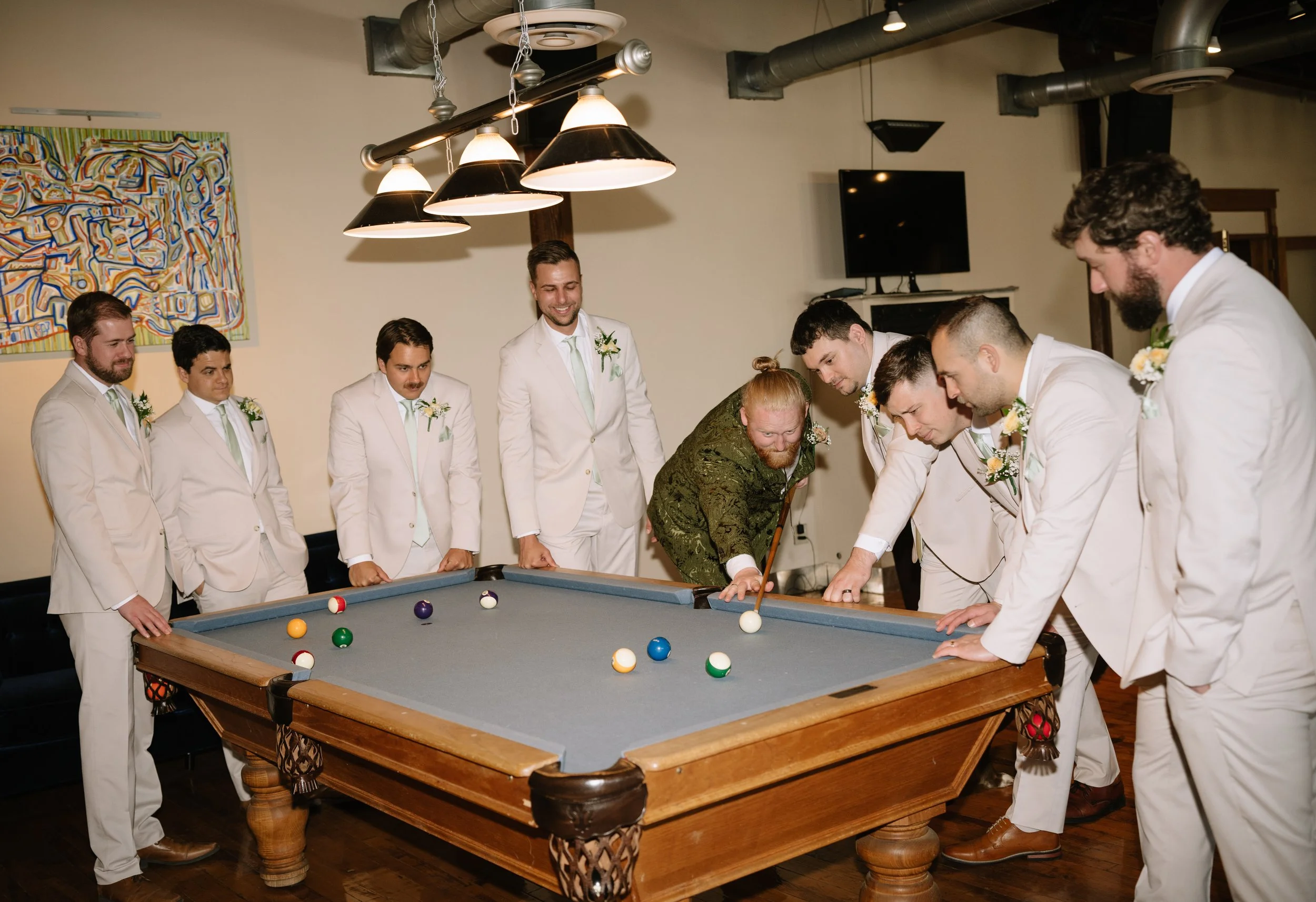 A group of men in white suits playing billiards at a decorated table in a room with modern art on the wall.
