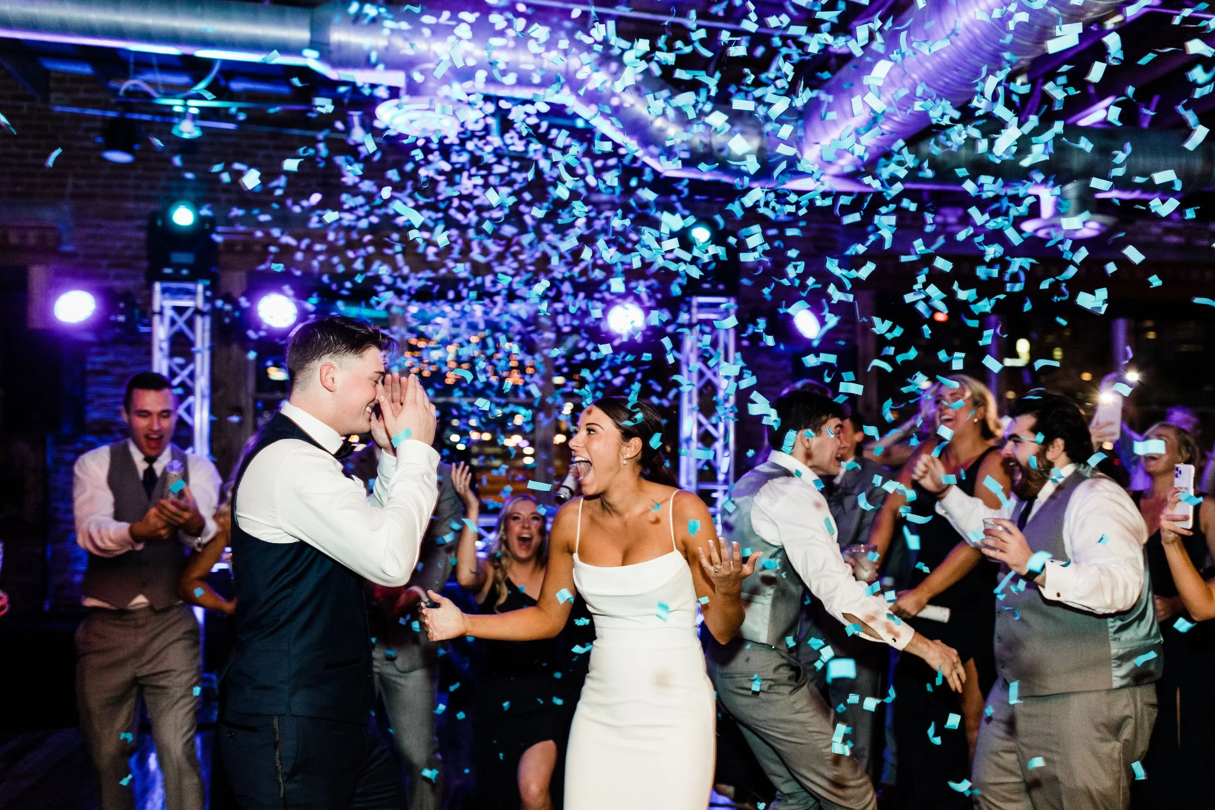 People celebrating at a wedding reception or party with confetti falling from the ceiling, dancing, and dressed in formal attire.