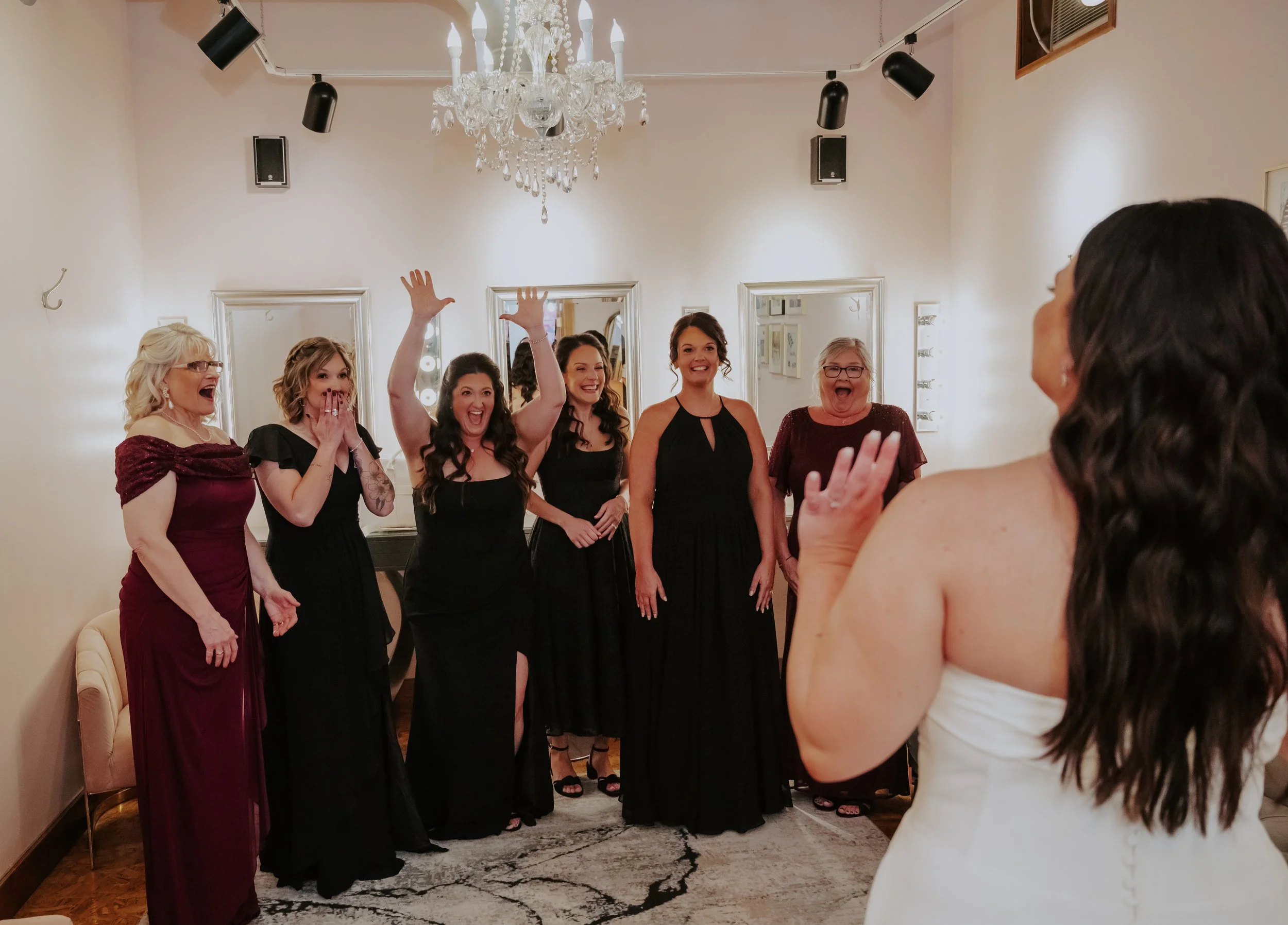 A group of women in formal dresses enjoying a celebration in a room with a chandelier and wall speakers.