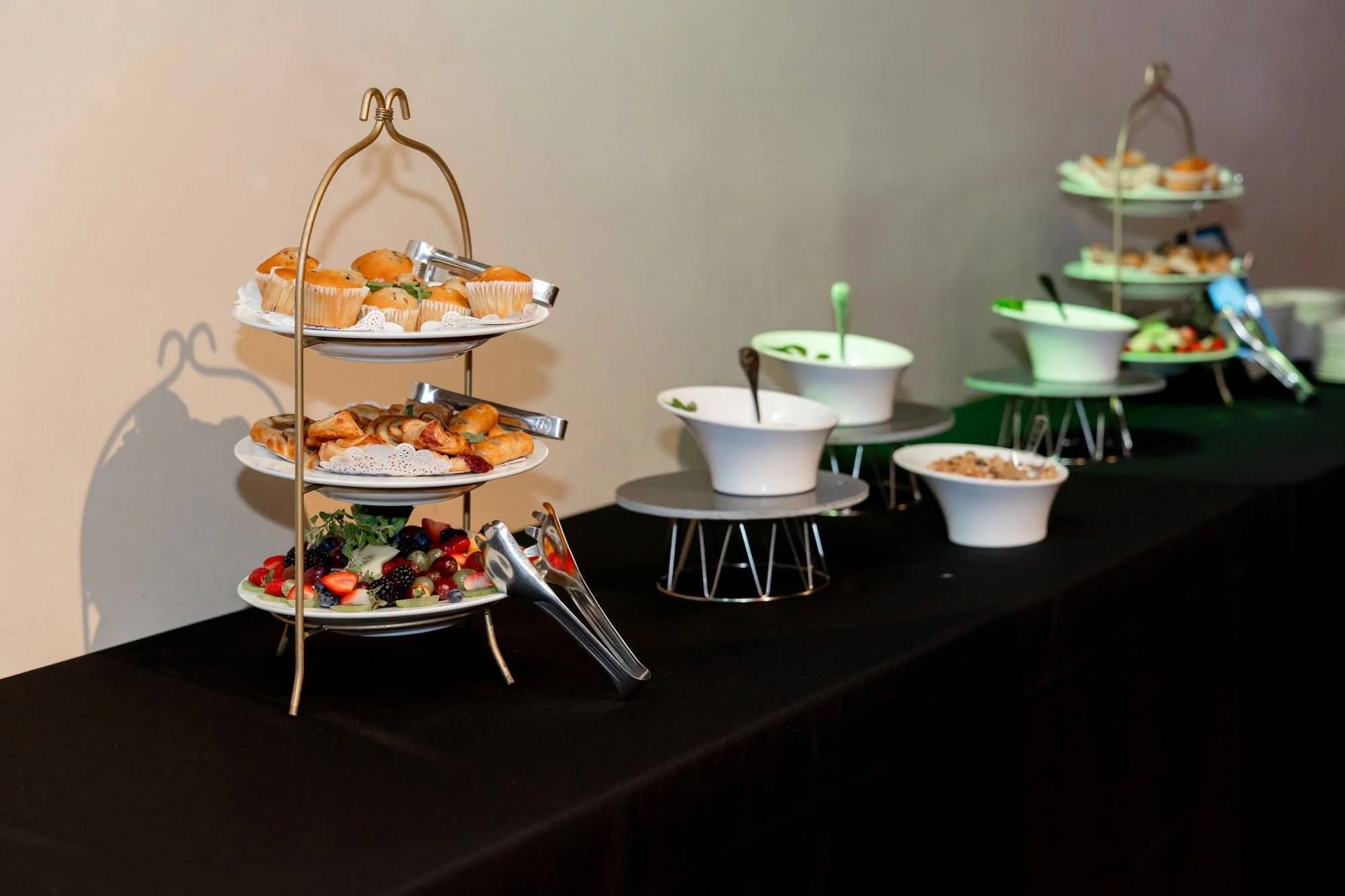 A dessert and salad buffet on a black table with multi-tiered fruit, pastry, and salad trays.