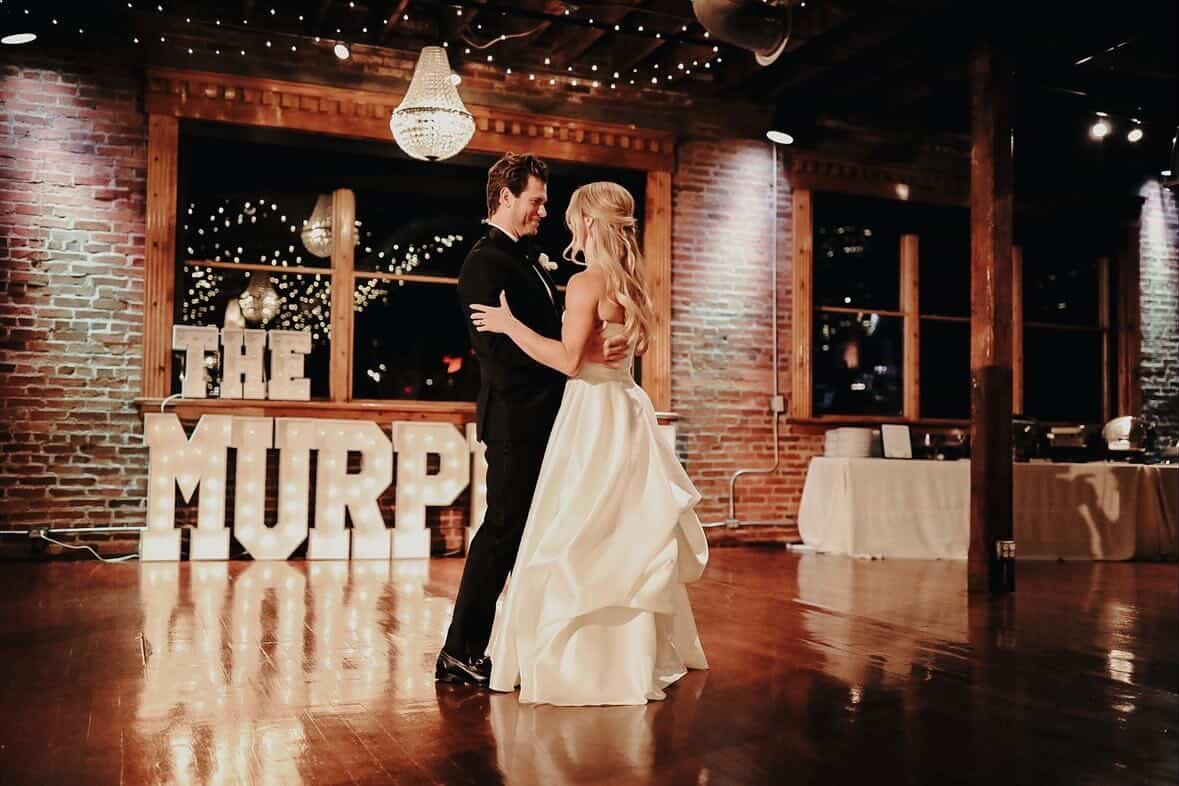 Bride and groom dancing in a rustic wedding venue with brick walls and string lights.