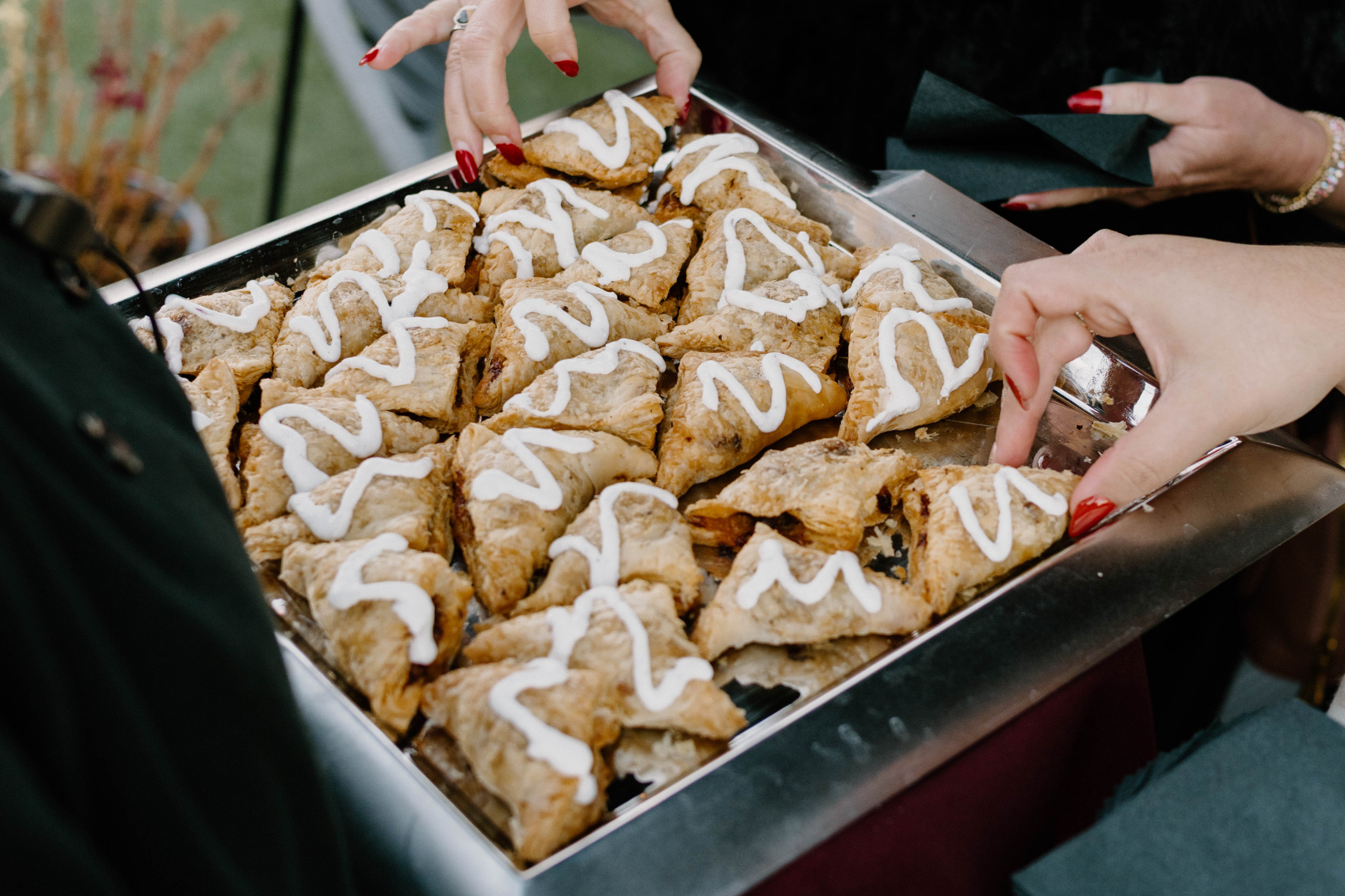 Close-up of a tray of cookies with white icing being picked up by hands with red painted nails.