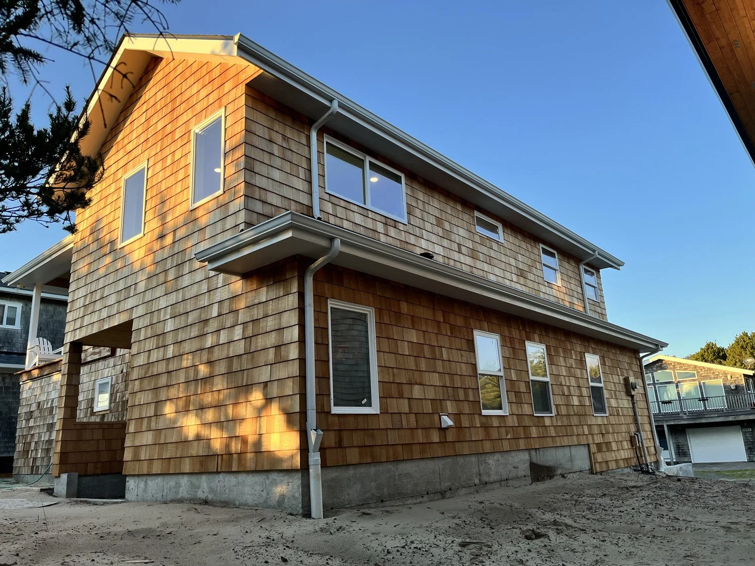 A two-story house with wooden shingle siding, multiple windows, and gutter system under a clear blue sky.