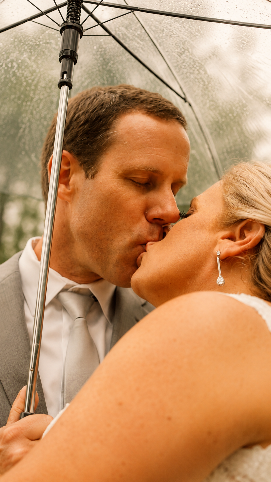 A bride and groom are kissing under an umbrella on a rainy day, close-up shot showing their faces and the umbrella.