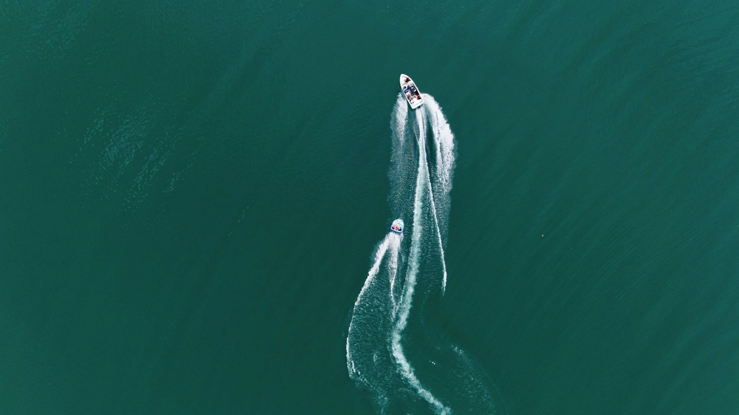 An aerial view of a boat traveling through a body of water, creating a trail of white wake behind it.