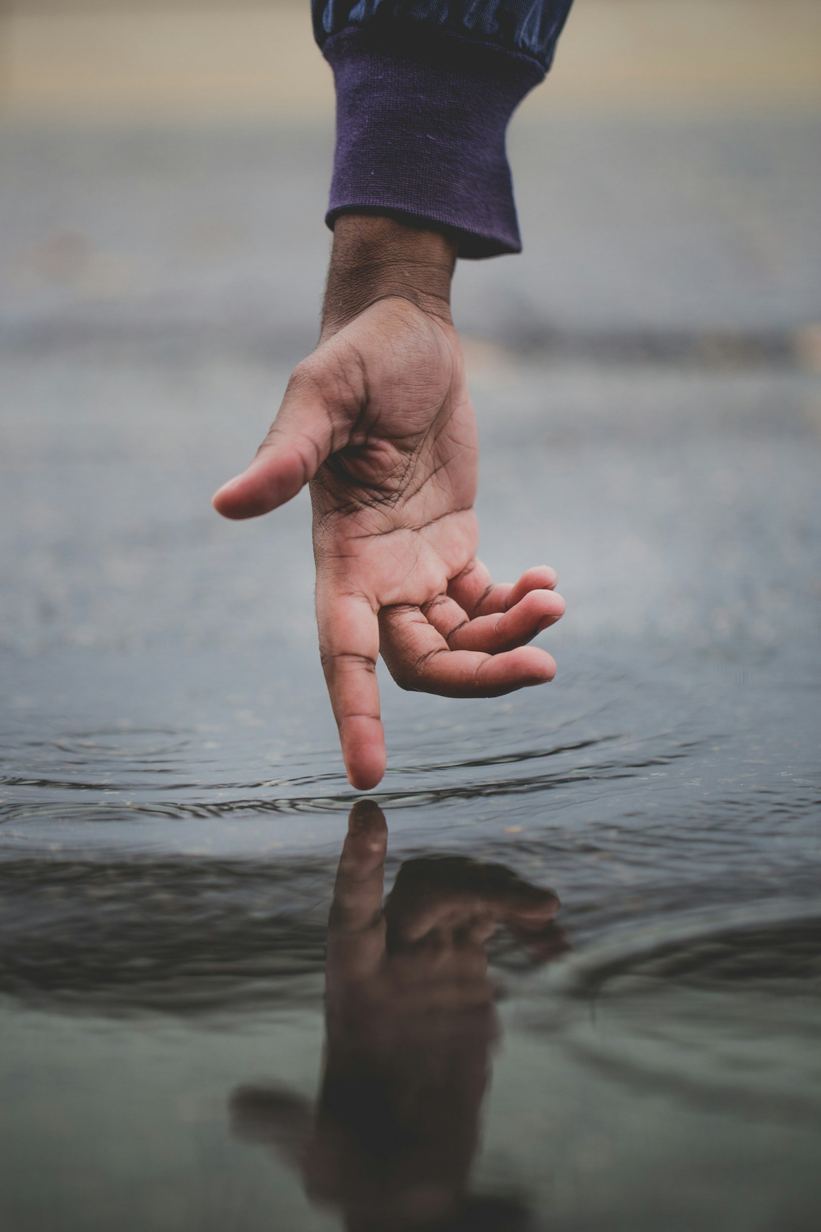 a hand palm out reaching to touch a rippling body of water with its four fingers