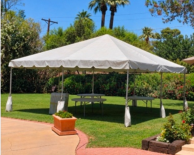 Outdoor event tent set up in a lush green garden with trees and flowers.