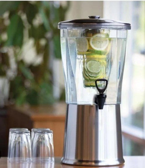 A glass beverage dispenser filled with water and sliced lemons and cucumbers, with two empty glasses nearby.