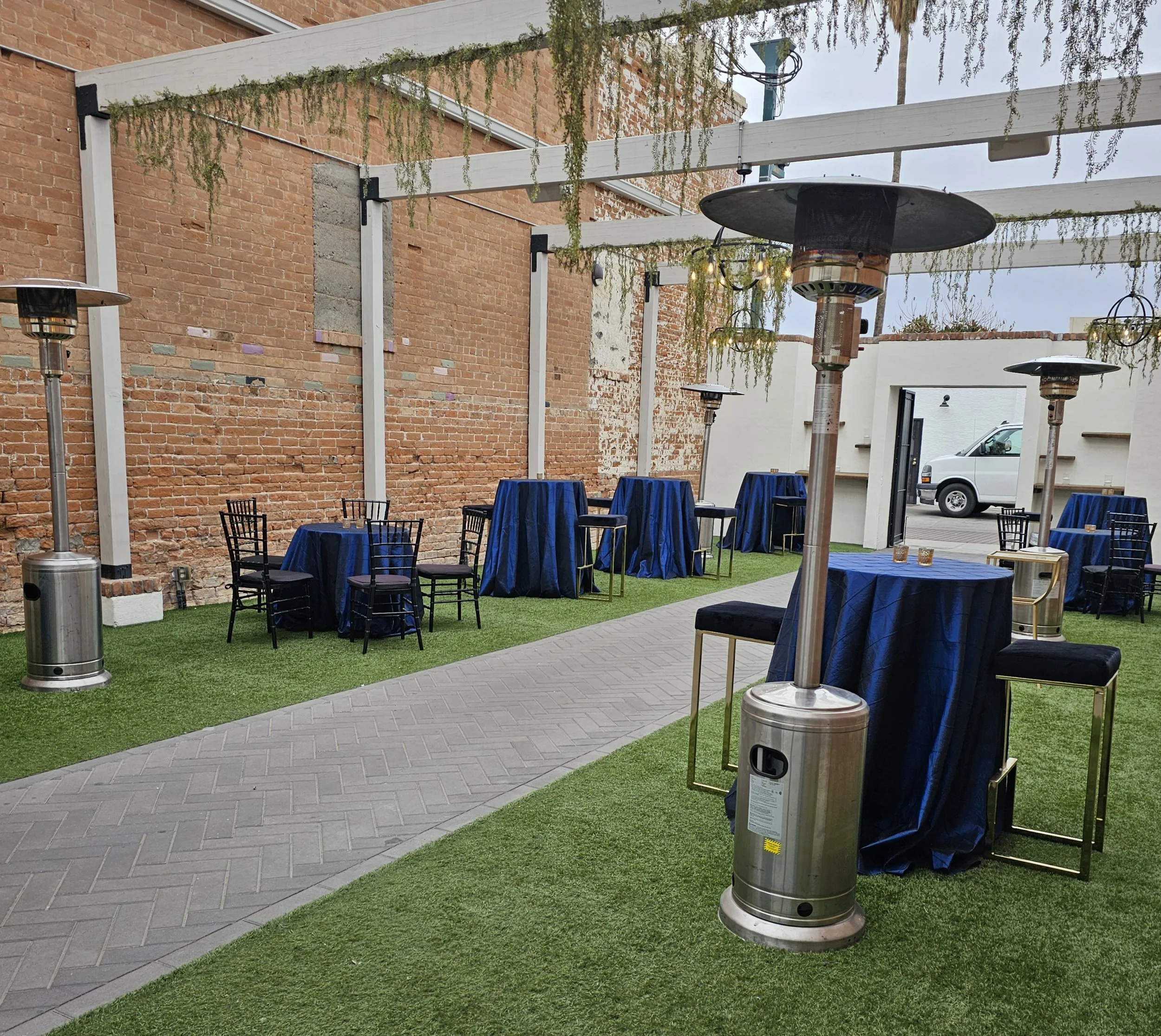 Outdoor event setup with cocktail tables, chairs and patio heaters under a pergola in Phoenix, Arizona.