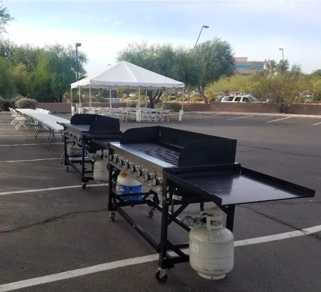 Outdoor event setup with gas grill rentals, folding tables and chairs, and a white canopy tent in Phoenix, Arizona.