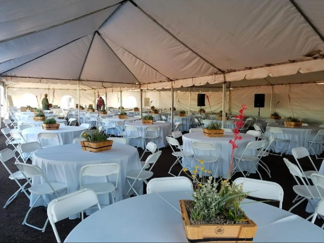 Event tent rental with round tables, white tablecloths and white folding chairs set up for a celebration in Phoenix, Arizona.