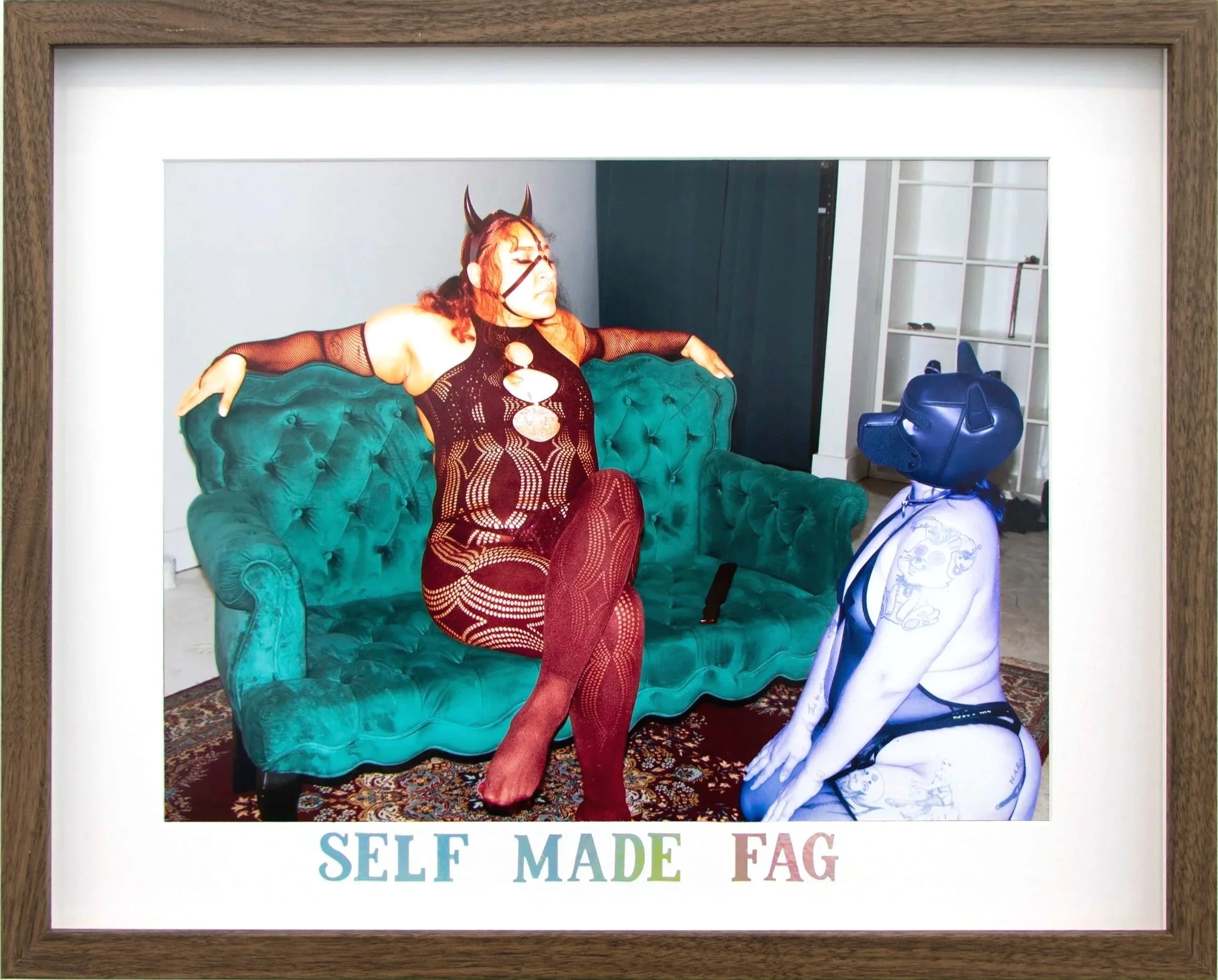 A person with horns and long red hair wearing a fishnet dress is sitting on a green tufted sofa with their arms stretched out, facing a police officer dressed in a white uniform and wearing a blue cap. A suitcase is on the floor next to the officer. 