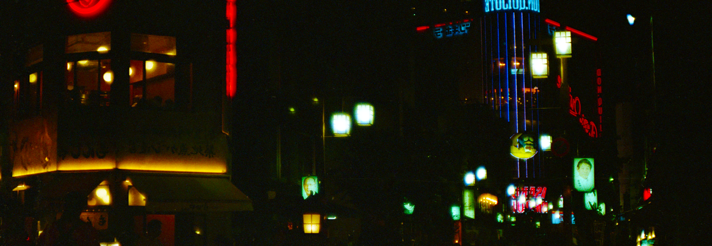 Night cityscape with illuminated signs and tall buildings featuring colorful neon lights and digital displays.