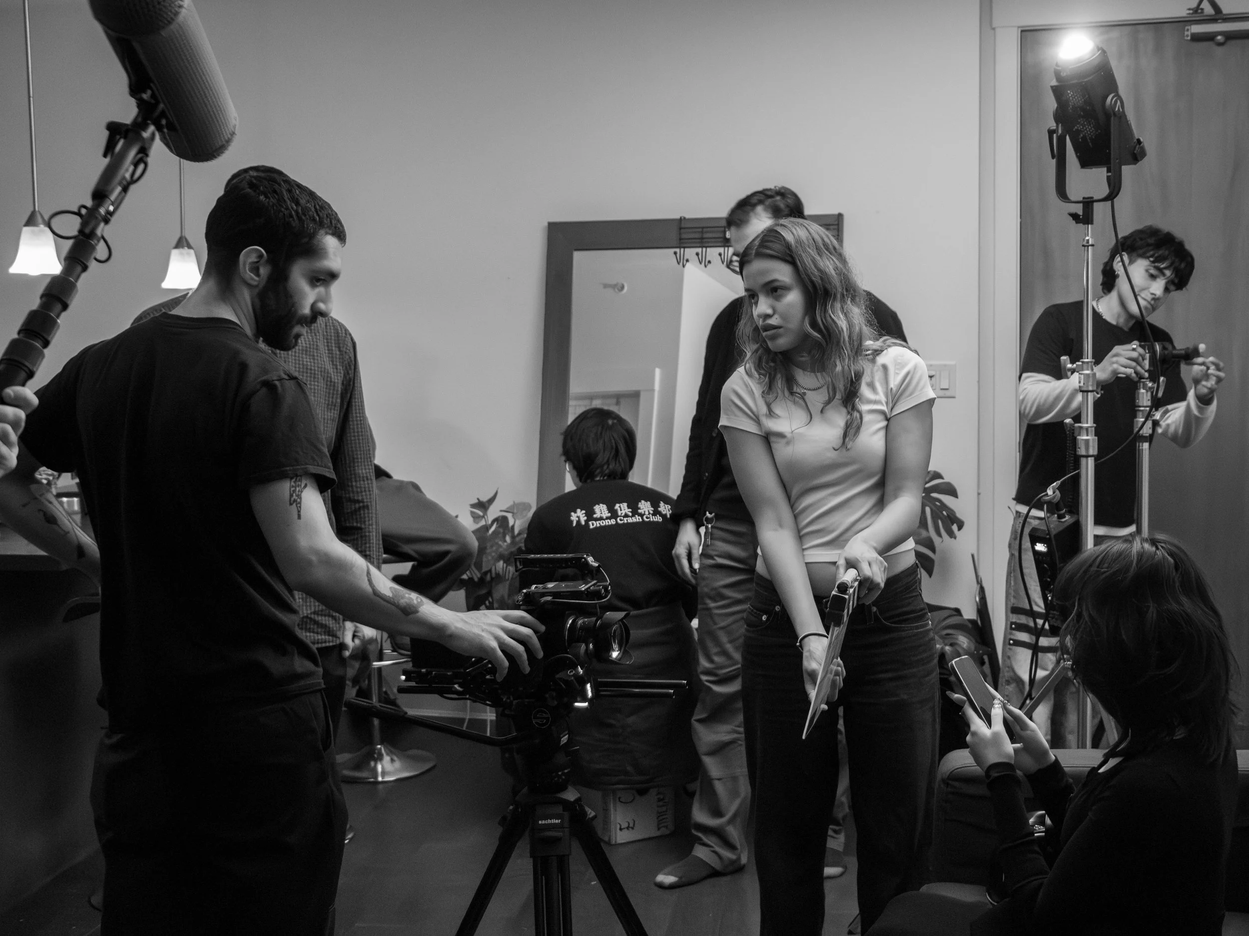 A group of people gathered around a camera on a tripod, working together on a film or photo shoot in an indoor setting.