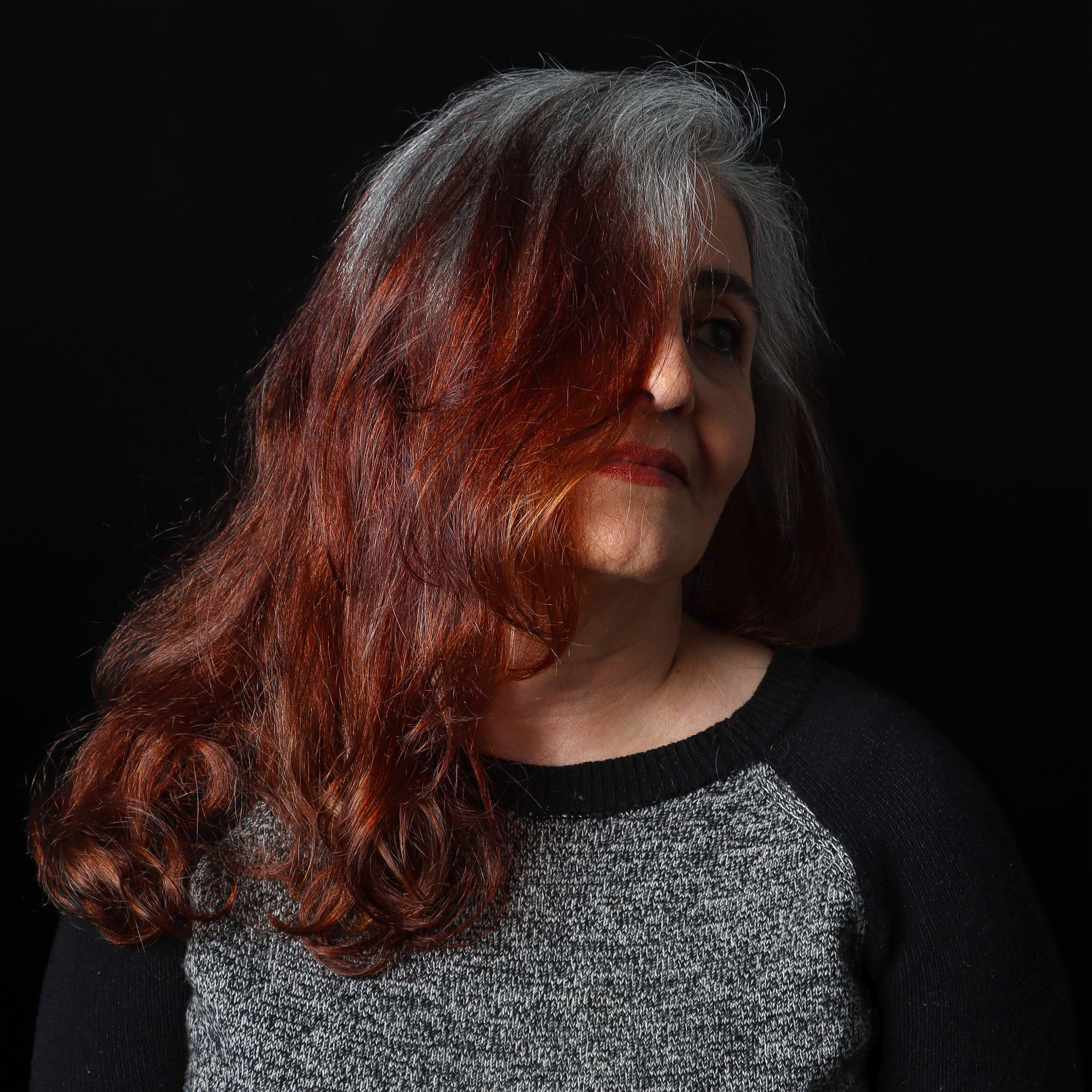 Close-up of a woman's face and hair with gray and red coloring against a black background.