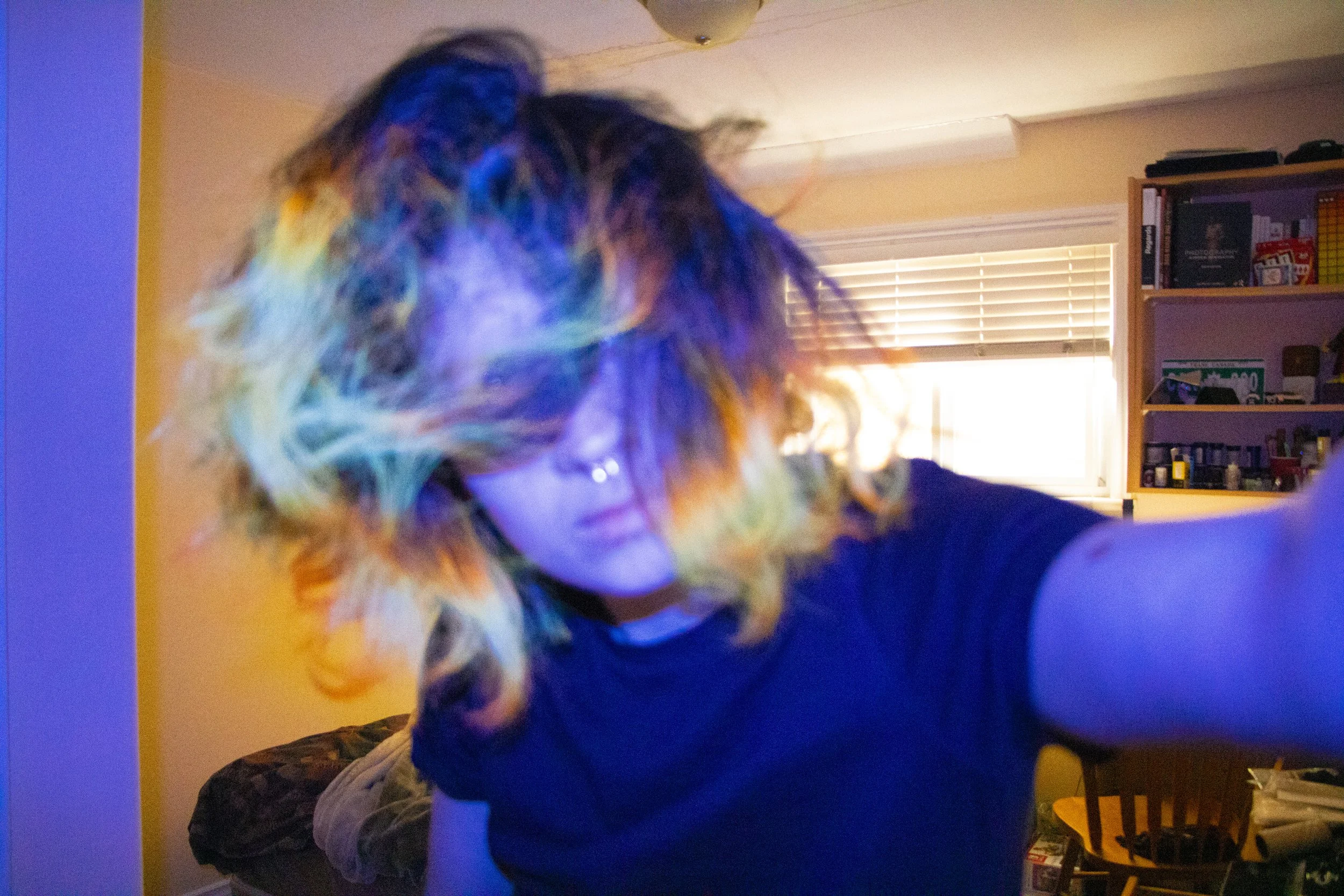 A close-up portrait of a person with colorful, UV lit, orange, yellow and brown hair covering their face