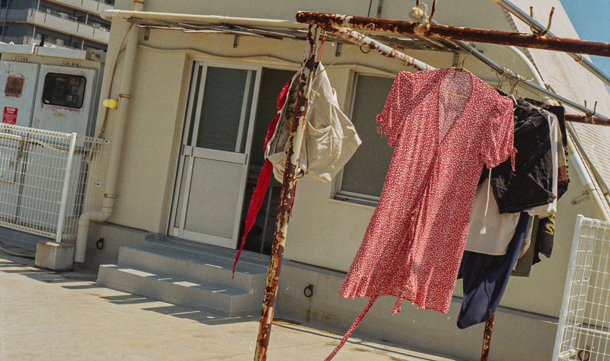 Clothes hanging on a rusty clothesline in a residential backyard, with a door and windows on a cream-colored house in the background.