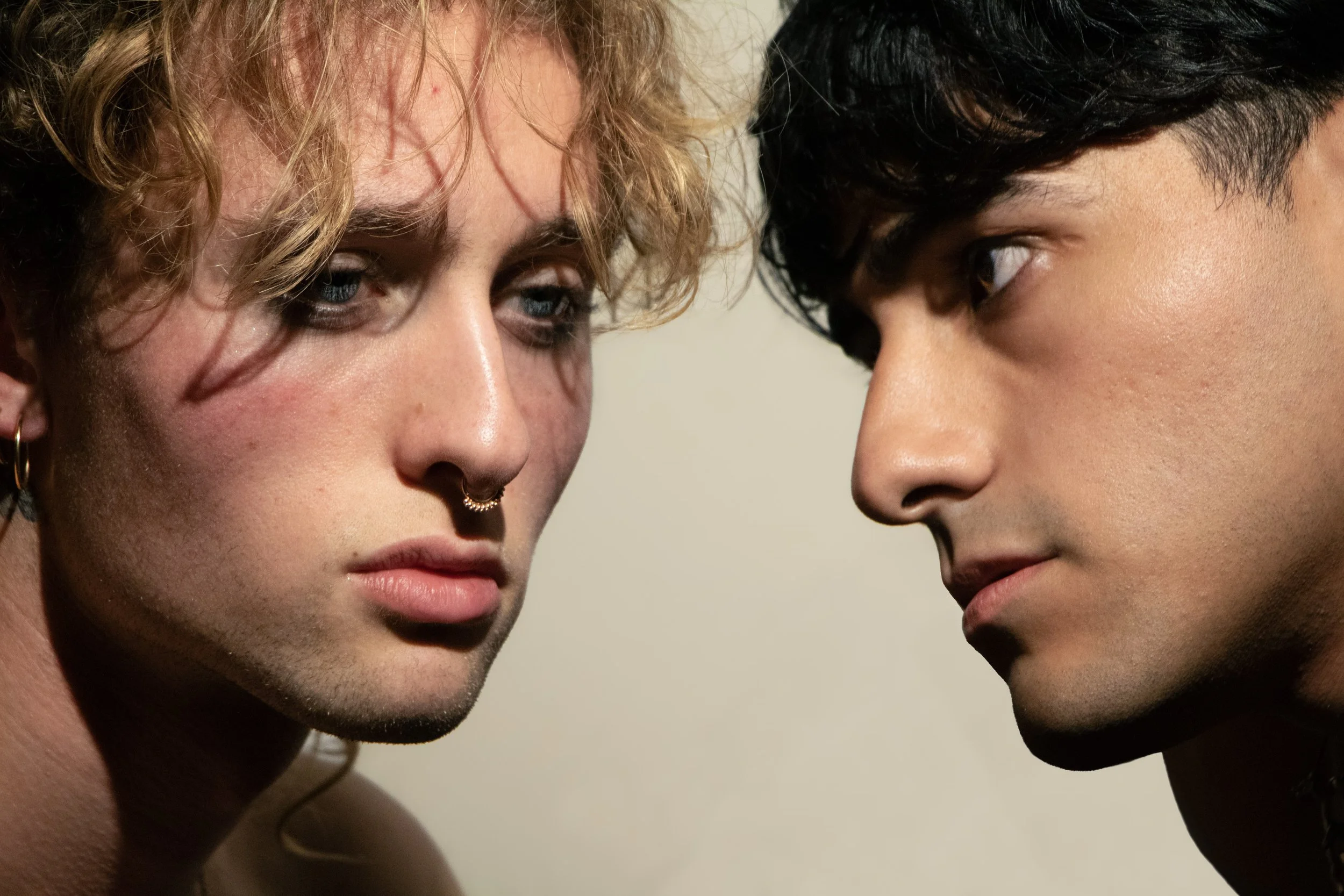 Close-up of two men with their foreheads and eyes nearly touching, with contrasting skin tones and hair types, gazing at each other.