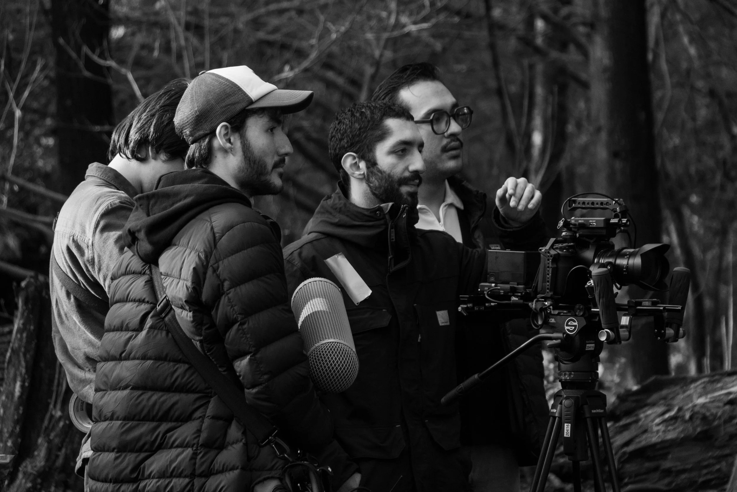 black and white image of four men on a film set outdoors, operating a professional camera on a tripod, with trees in the background.