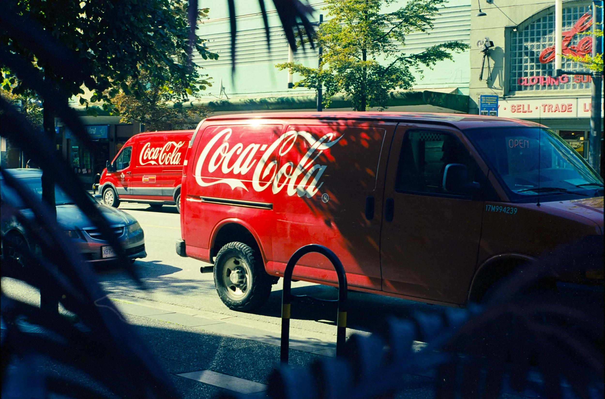 Red Coca-Cola delivery vans parked along a street with trees and buildings in the background.