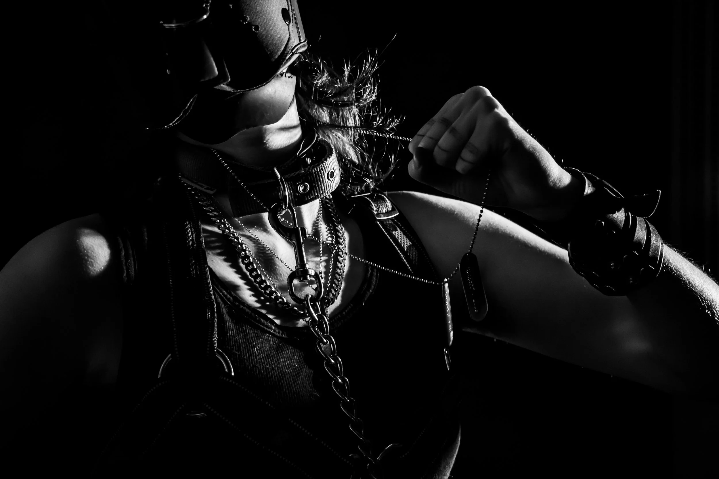 A person wearing sunglasses and layered necklaces, holding a chain in their hand, captured in black and white with dramatic lighting.