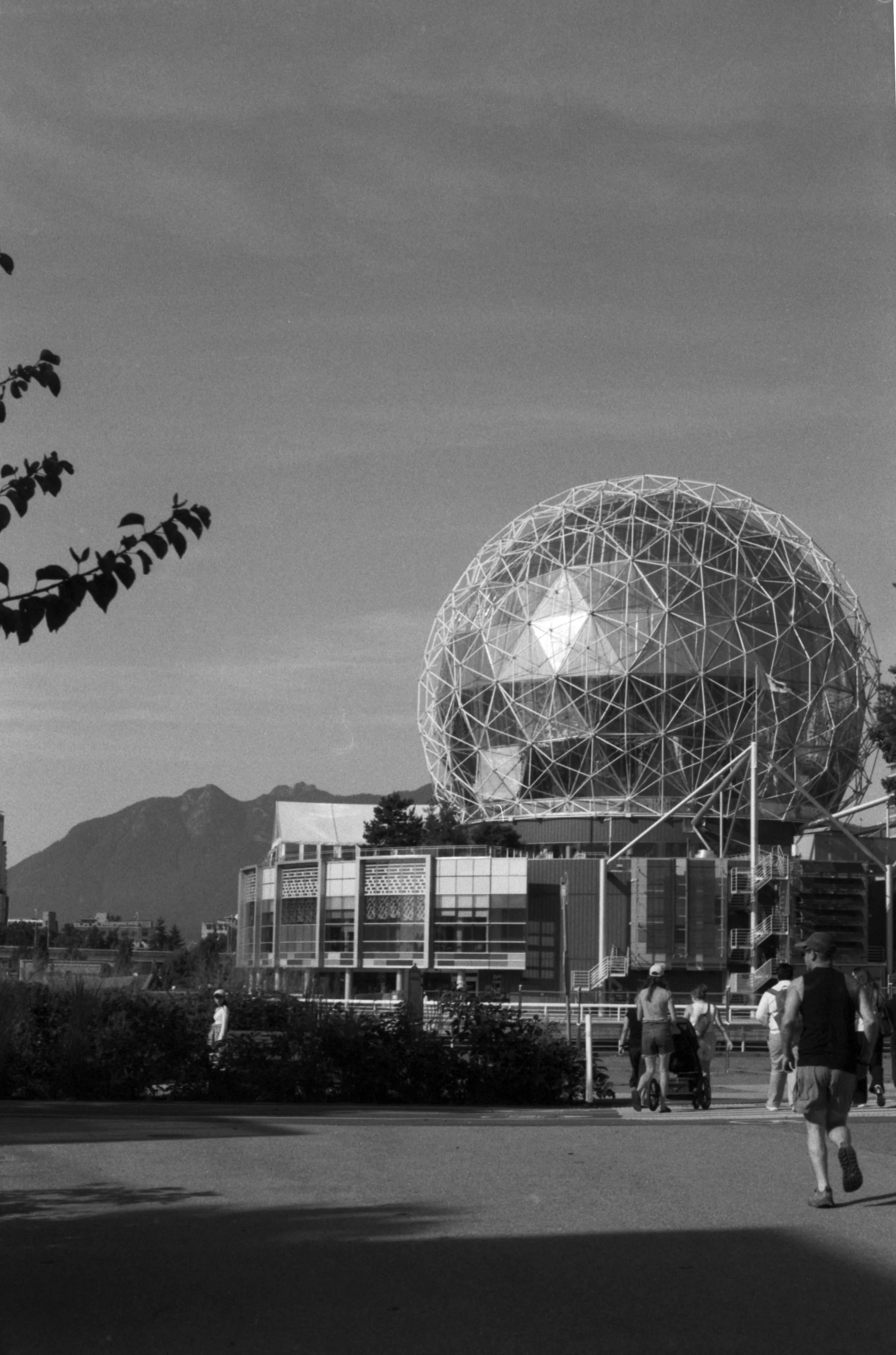A black-and-white photo of Science-World in Vancouver, mountains in the background, and people walking in the foreground.