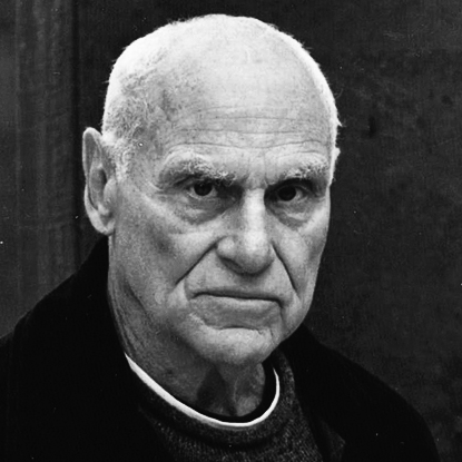Close-up black-and-white photo of an elderly man with a serious expression, short white hair, and wearing a dark coat.