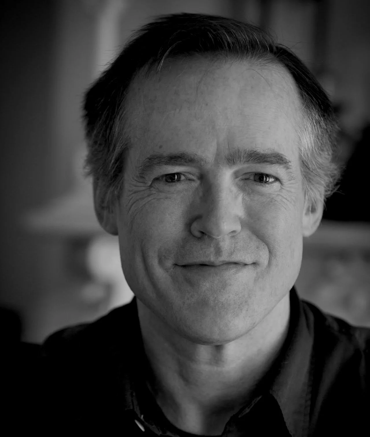 Black and white close-up portrait of a smiling Scott Moyers, wearing a dark jacket, looking directly at the camera.