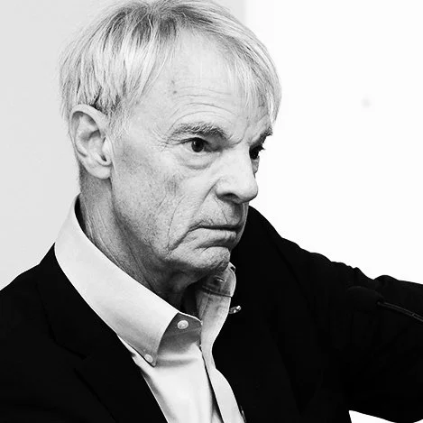 Black and white photo of Michael Spence, wearing a suit and collared shirt, looking to the side with a serious expression.